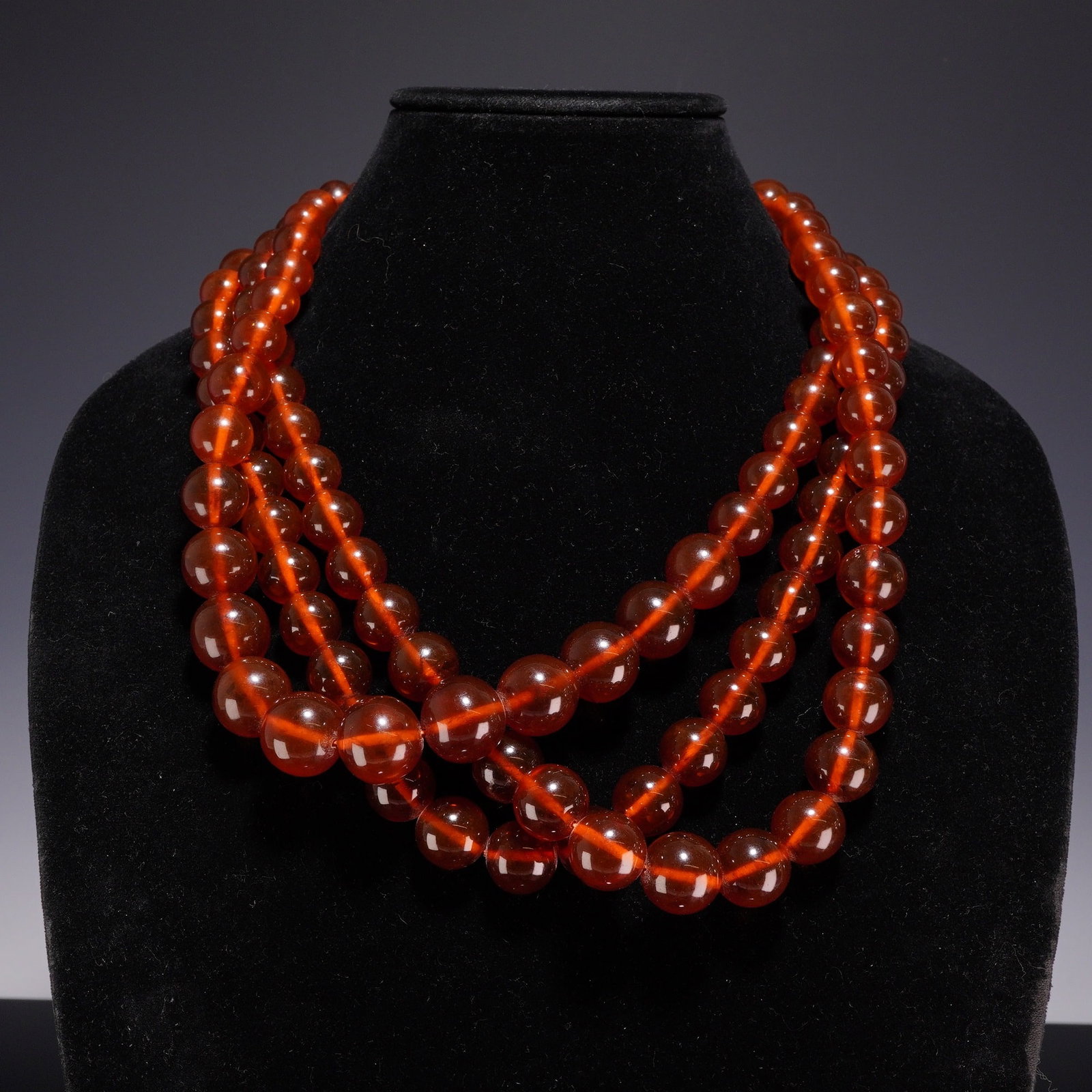 3pc Graduated Amber Bead Costume Jewelry Necklaces: This lot features three graduated bead necklaces identified as costume jewelry. The beads are composed of translucent amber-colored material ranging in shade from deep orange to reddish-brown. Each ne