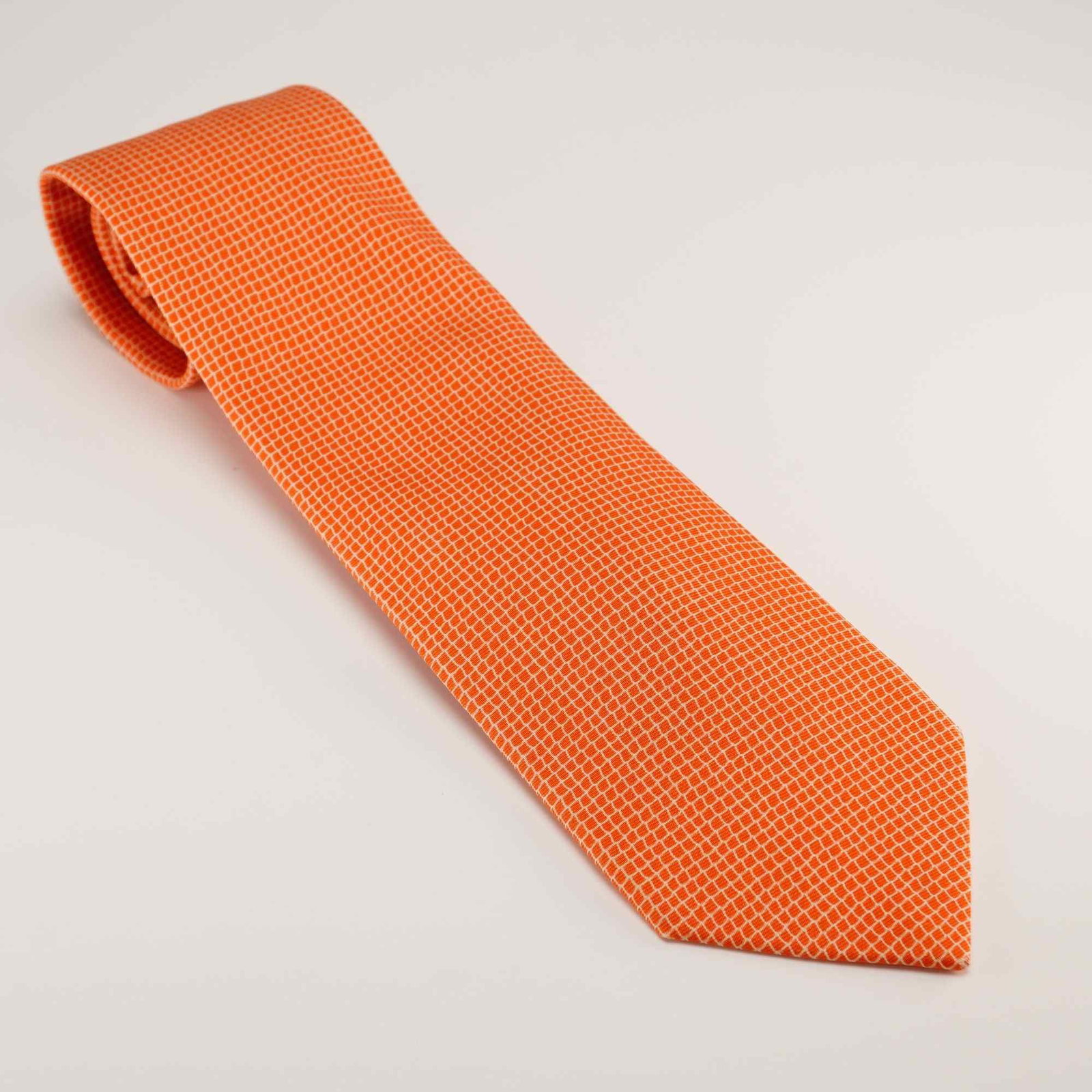 Hermes Paris 100% Silk Gentlemen's Tie with Orange Geometric Pattern: An authentic Hermes Paris 100% silk gentlemen's necktie featuring a vibrant orange ground decorated with a repeating small-scale white geometric grid pattern. The reverse of the tie includes a woven d