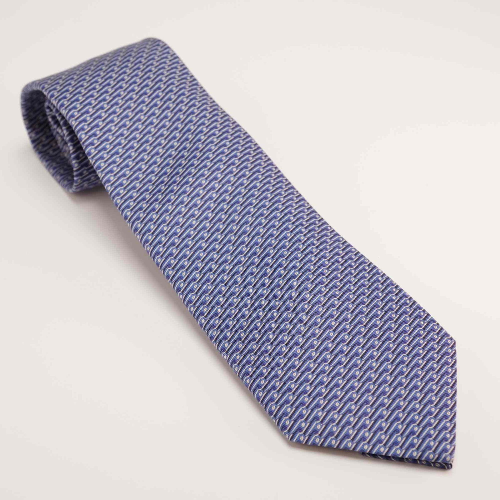 Hermes Paris 100% Silk Gentlemen's Tie with Uncommon Motorboat Graphic: This Hermes men's necktie is constructed from 100% silk and features a tonal blue and white repeating geometric pattern. A notable and uncommon design element is located on the reverse of the wide bla