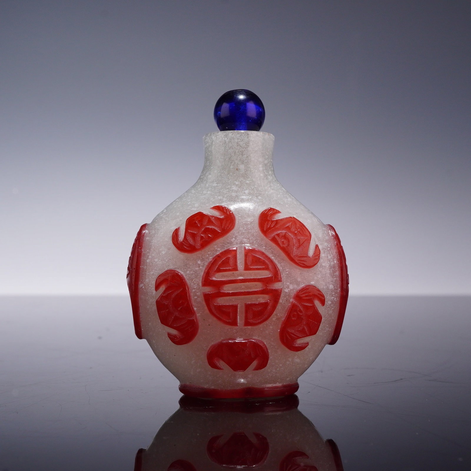 Chinese Carved Red Overlay Snowflake Glass Snuff Bottle with Stopper: A Chinese snuff bottle of flattened globular form with a short cylindrical neck and a recessed oval base. The body is constructed of snowflake glass, characterized by translucent white glass containin