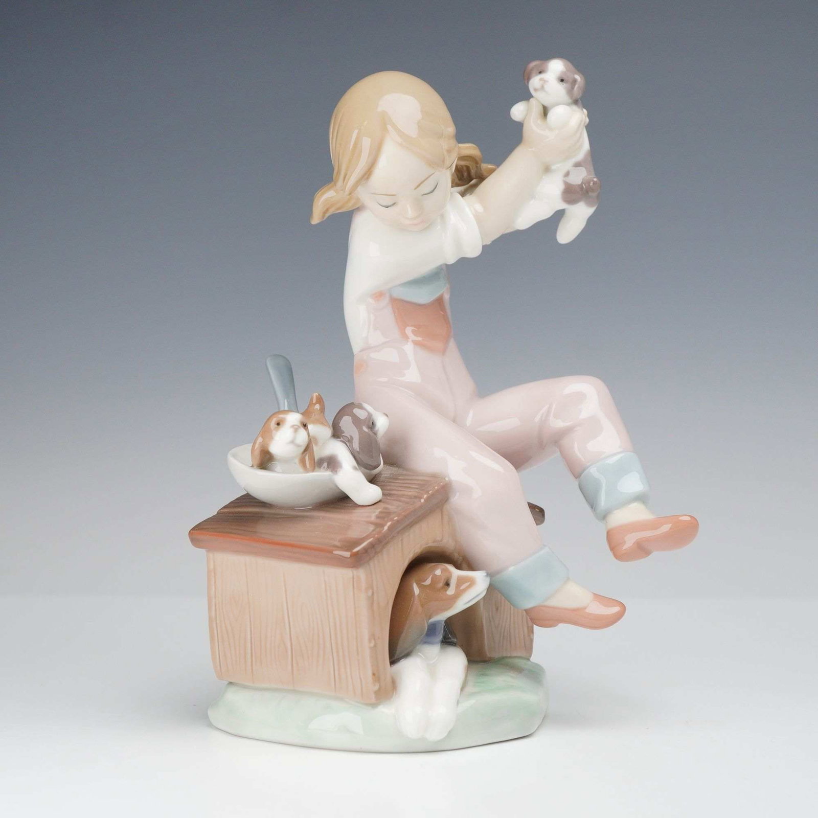 Lladro Glazed Porcelain Figurine Pick of the Litter 01007621 with Box: This authentic Lladro glazed porcelain figurine depicts a young girl with blonde pigtails dressed in pink overalls over a white shirt. The figure is seated atop the roof of a wood-textured doghouse, h