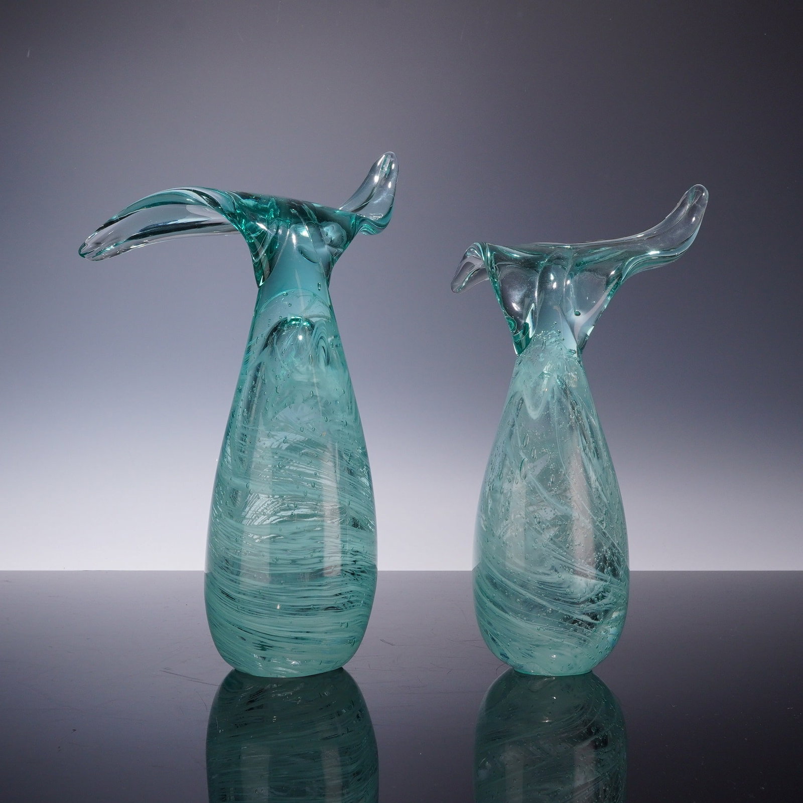 A Pair of Tozai Home Hand-Blown Art Glass Whale Tail Figurines: This lot features a pair of contemporary art glass vases produced by Tozai Home. Each piece is hand-blown into a sculptural whale tail form, characterized by a teardrop-shaped vessel that extends into
