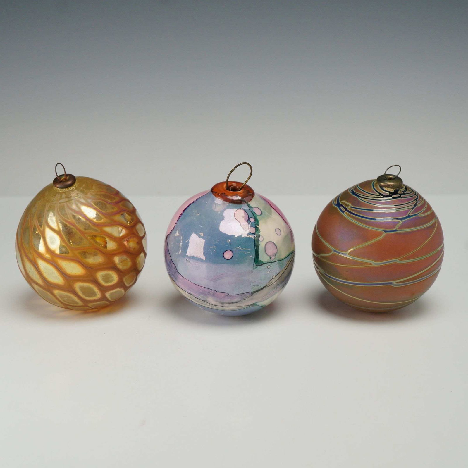 Three Craig Zweifel Signed Hand-Blown Iridescent Art Glass Ornaments: Three hand-blown art glass ornaments by Craig Zweifel. The collection features three distinct designs showcasing various iridescent glass techniques. The first ornament is crafted with a golden-amber 