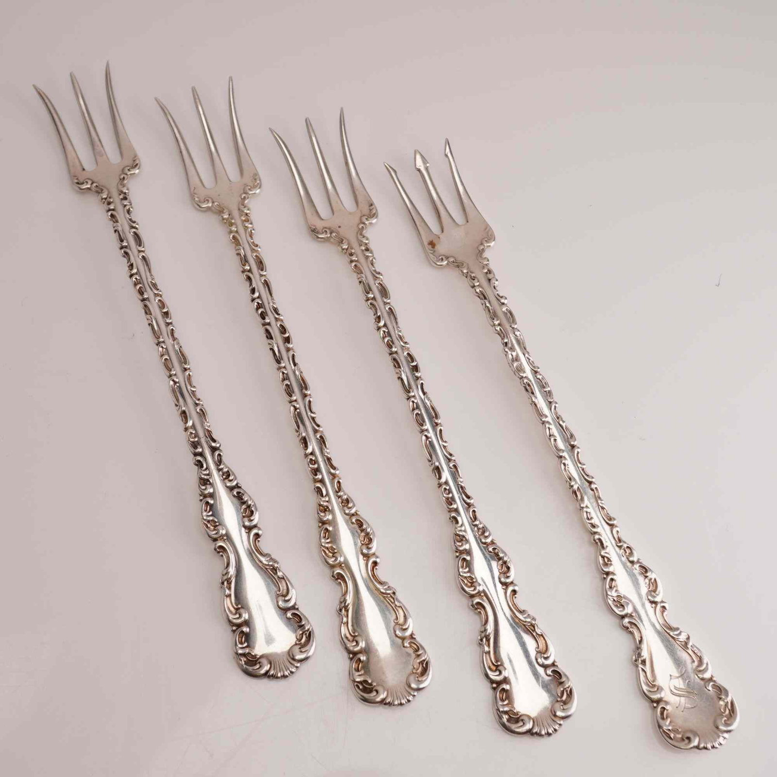 4pc Whiting Manufacturing Company Sterling Silver Cocktail Forks, Louis XV: A set of four sterling silver three-tine forks in the Louis XV pattern by the Whiting Manufacturing Company. These cocktail forks feature an ornate Rococo Revival design characterized by elaborate scr