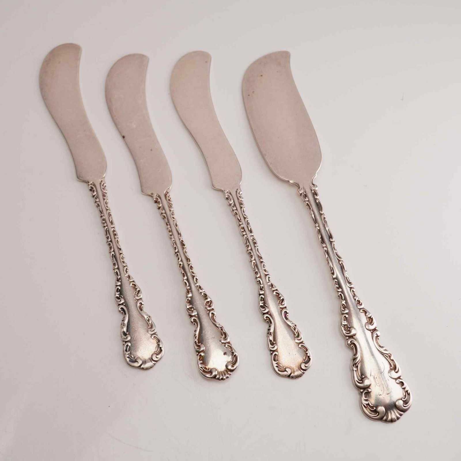 4pc Whiting Manufacturing Company Sterling Silver Butter Knives, Louis XV: A set of four sterling silver butter knives in the Louis XV pattern by the Whiting Manufacturing Company. This collection consists of one larger master butter knife and three individual flat-handle bu