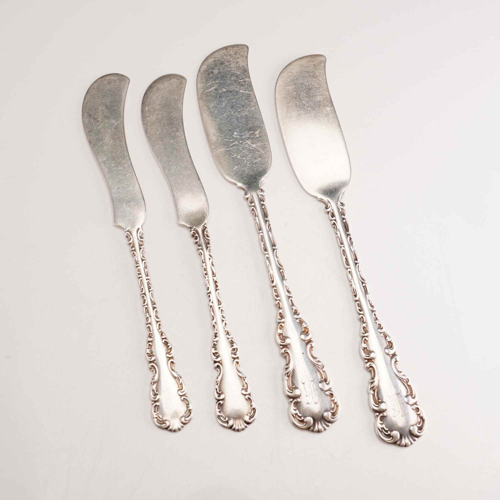 4pc Whiting Manufacturing Company Sterling Silver Butter Spreaders, Louis XV: A group of sterling silver flatware pieces in the Louis XV pattern by Whiting Manufacturing Company, patented in 1891. The collection consists of four all-silver butter spreaders featuring two distinc