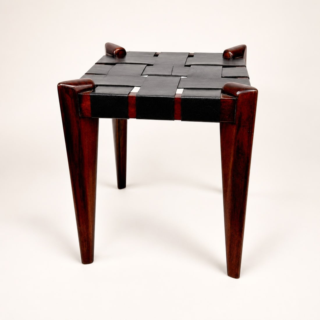 Mid-Century Modern Woven Leather and Hardwood Stool in the Style of Edmond Spence: This mid-century modern footstool or ottoman is designed in the style of American designer Edmond J. Spence, dating to the circa 1950s. The piece features a square frame constructed from a dark,