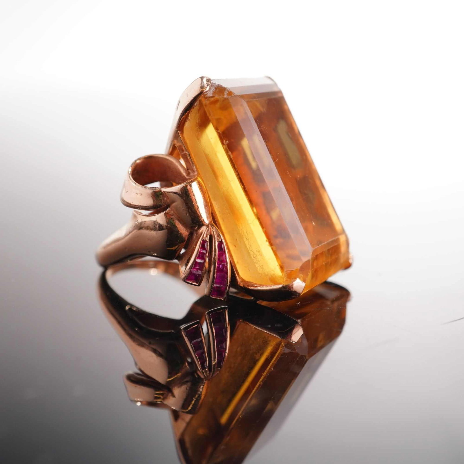 12 Karat Yellow Gold Citrine and Ruby Cocktail Ring: This Retro period cocktail ring, is constructed from tested 14 karat yellow gold. The ring features a large, emerald-cut citrine of a warm yellow-orange tone, secured in a substantial four-prong
