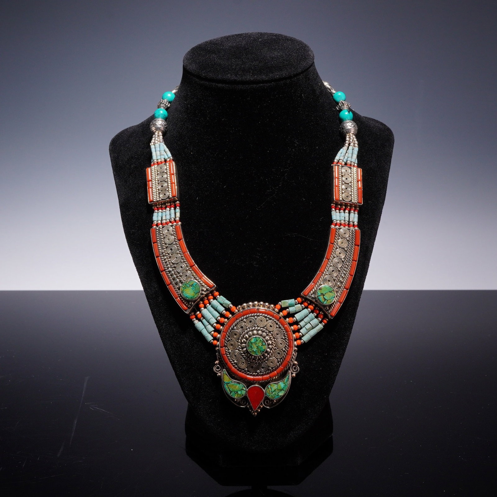 Tibetan-Style Multi-Strand Turquoise and Coral Costume Bib Necklace: A large Tibetan-style multi-strand bib or collar costume necklace. The necklace is constructed from silver-toned metal featuring intricate wirework filigree, spiral motifs, and granulation. The