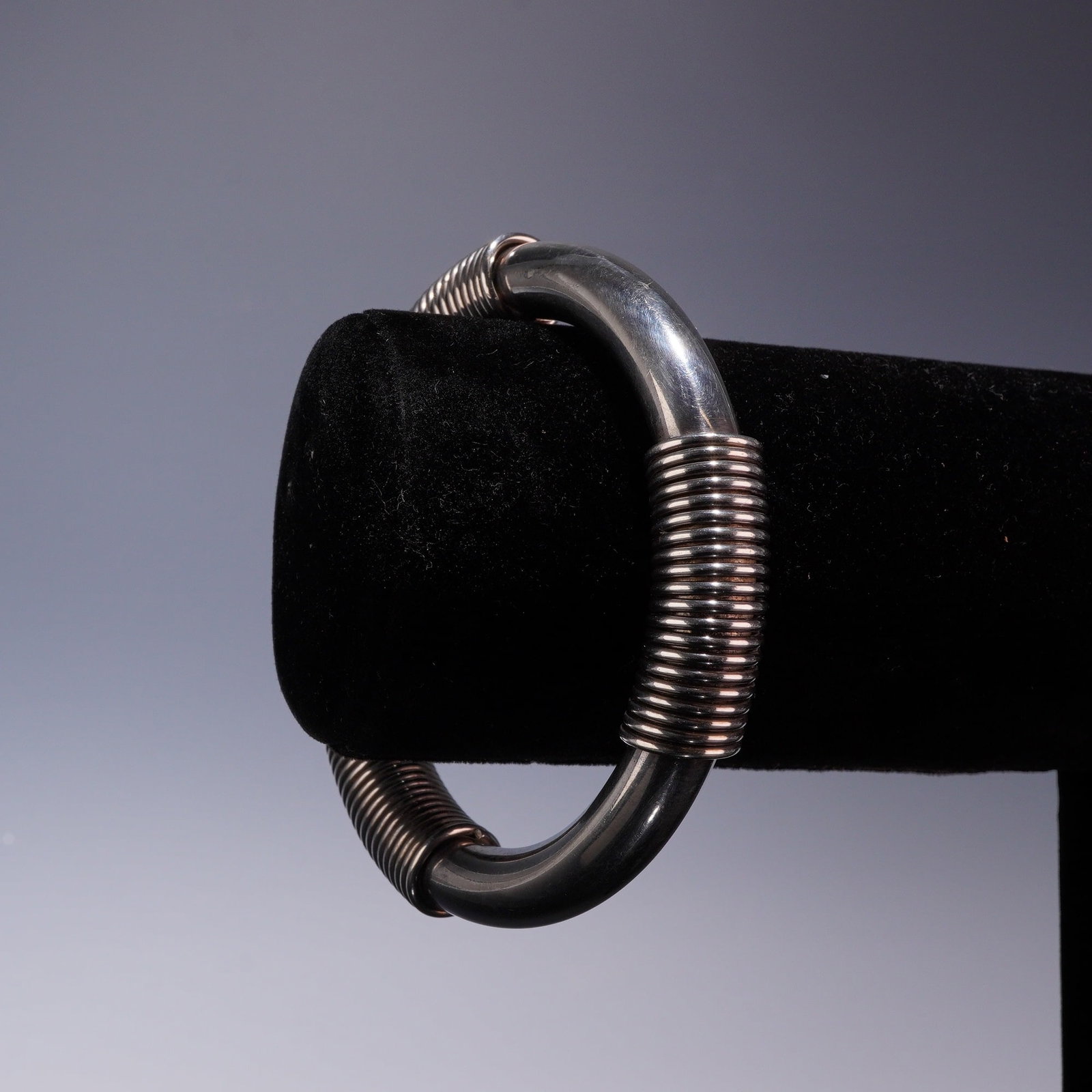 Sterling Silver Tubular Bangle Bracelet with Coiled Wire Wrap: This sterling silver bangle bracelet features a polished tubular form embellished with three distinct sections of tightly coiled wire wrap. The piece is a continuous, slip-on style without a clasp or