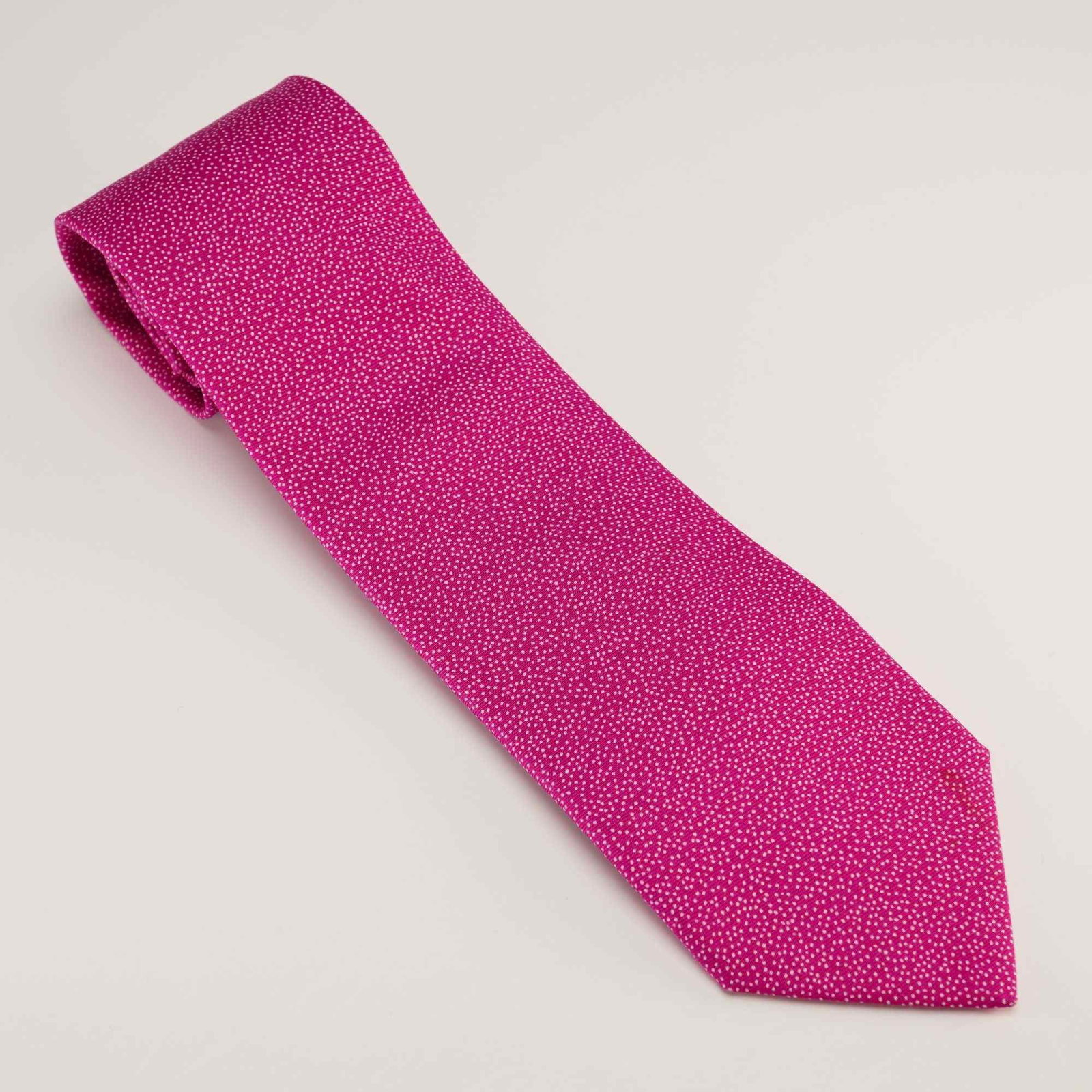 Hermes Paris 100% Silk Gentlemen's Tie: This gentlemen's necktie by Hermes, Paris is crafted in France from 100% silk. The design features a fuchsia pink ground decorated with an all-over white pinpoint speckled polka dot pattern. The rever