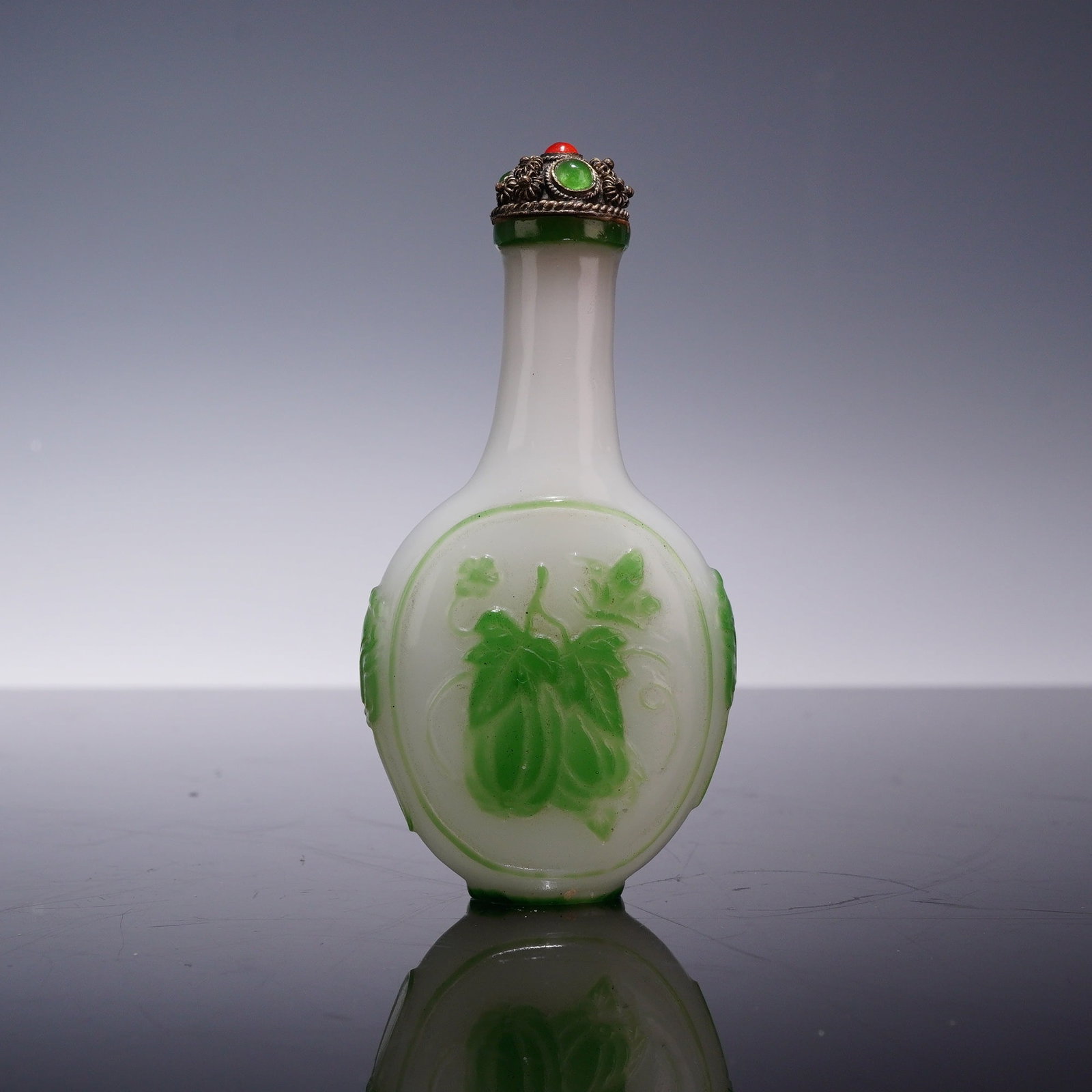 Chinese Green Overlay Peking Glass Snuff Bottle with Stopper: A Chinese Peking glass snuff bottle featuring a flattened ovoid body and a tall, slender cylindrical neck. The bottle is constructed from an opaque milky white glass base with an emerald green glass o