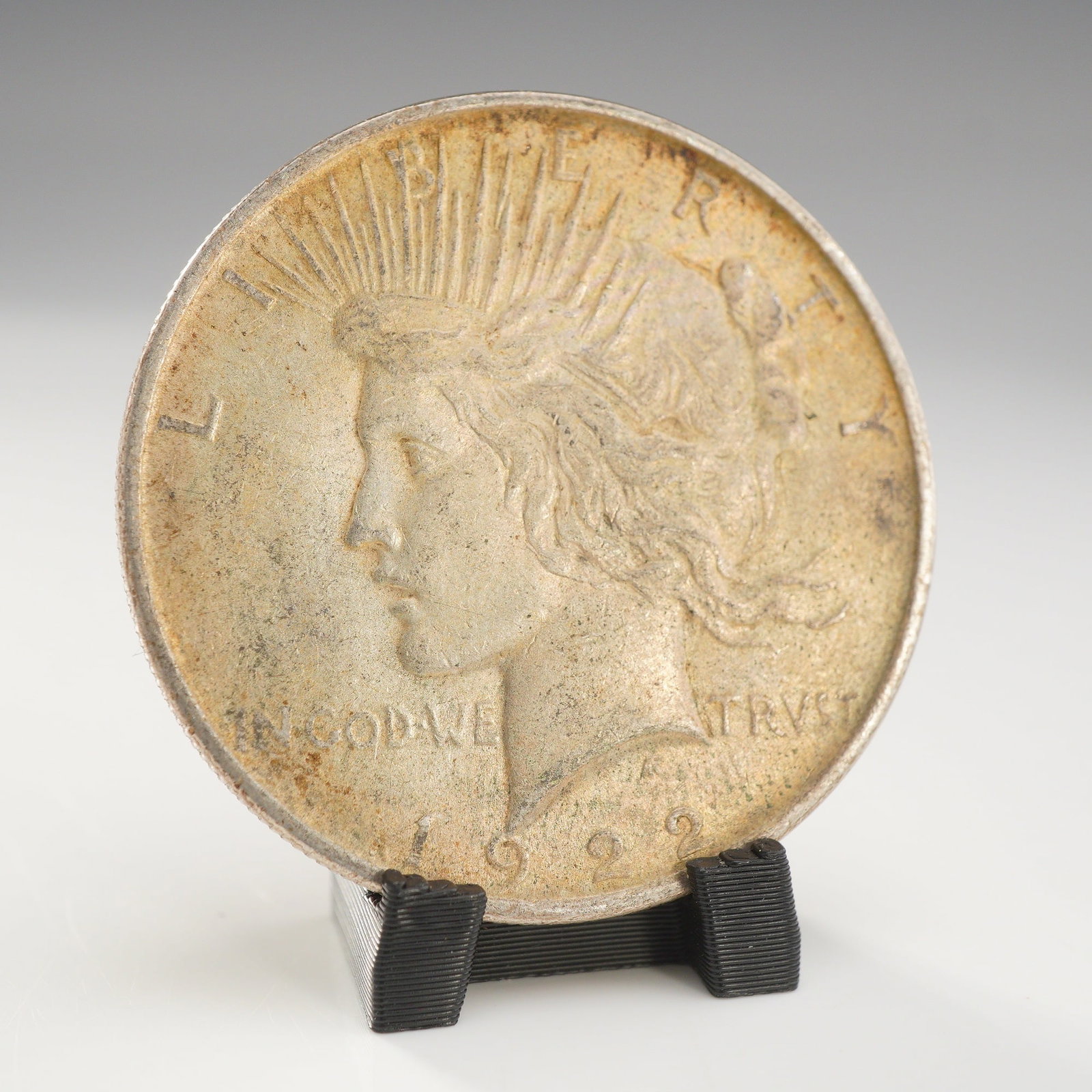 1922 US Peace Silver One Dollar Coin, Circulated: This 1922 US Peace silver dollar is struck in a 90% silver composition. The coin features the Liberty head obverse and the eagle reverse design types. No mint mark is present, identifying the