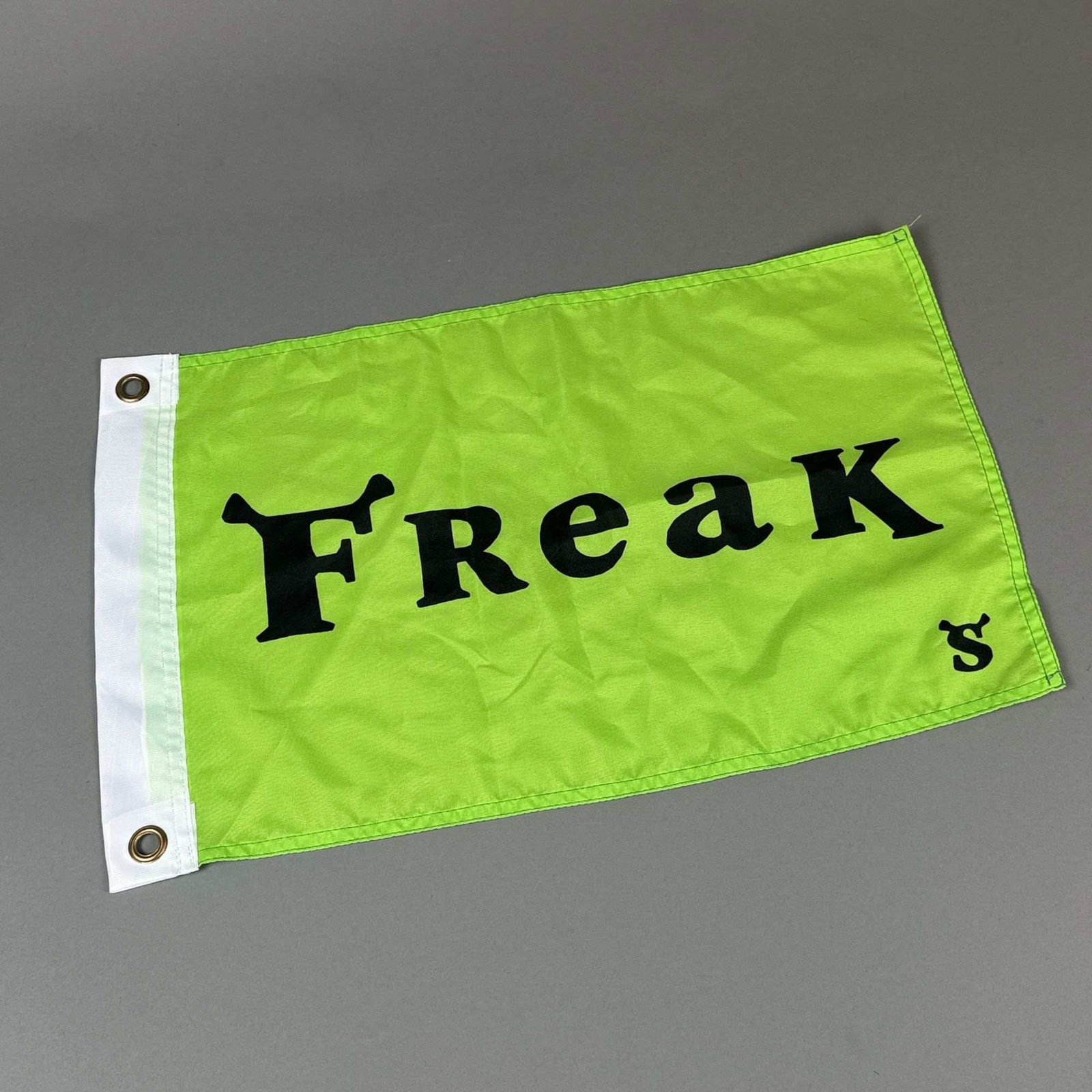 Shrek The Musical Broadway Freak Flag: A novelty flag associated with the Broadway production of Shrek The Musical. The rectangular banner is composed of bright lime green synthetic fabric and features the word Freak printed in black. The