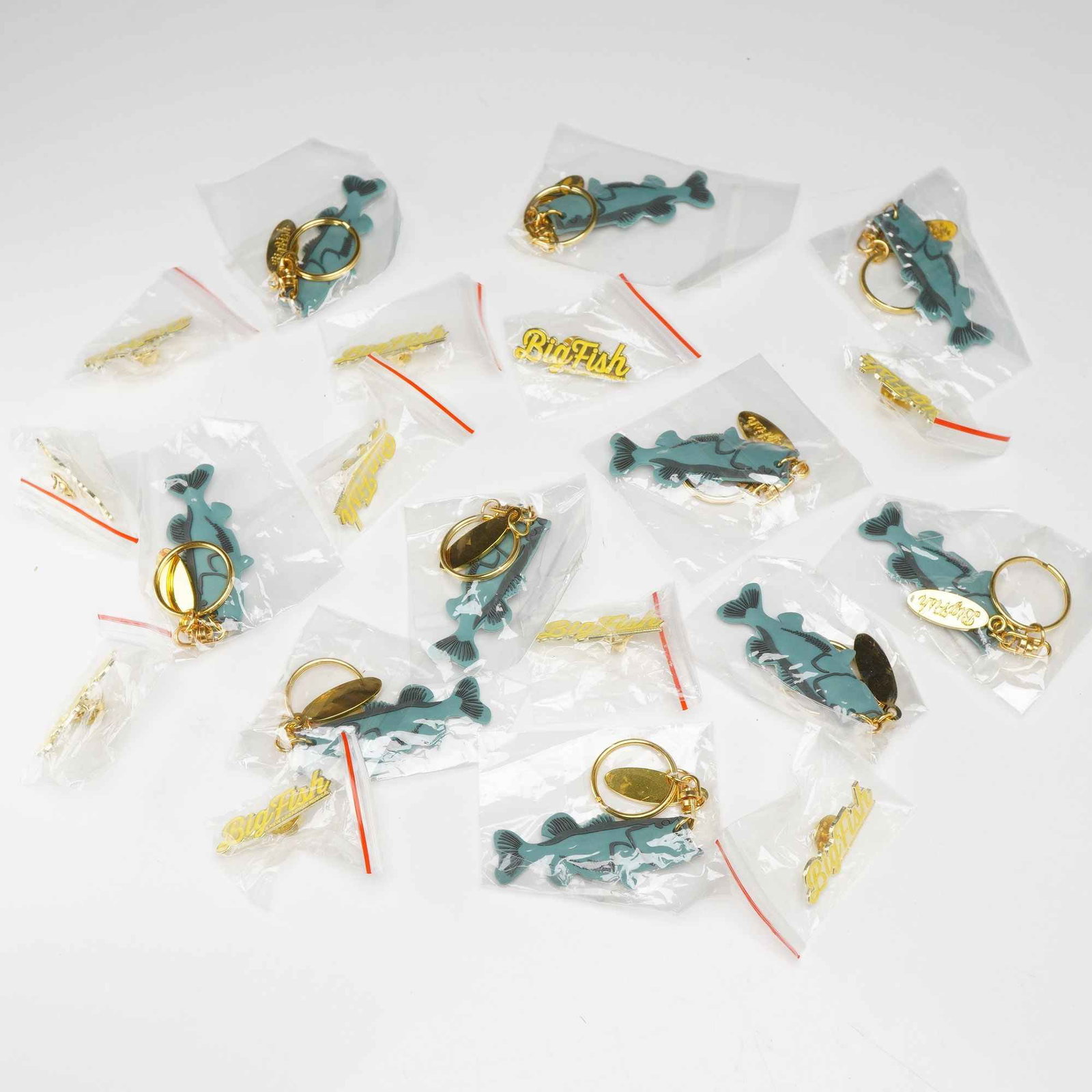 20pc Lot of Big Fish Broadway Musical Keychains and Pins: A collection of promotional merchandise from the 2013 Broadway musical Big Fish. This lot includes 10 keychains and 10 enamel lapel pins. The keychains feature a molded teal and grey silicone charm