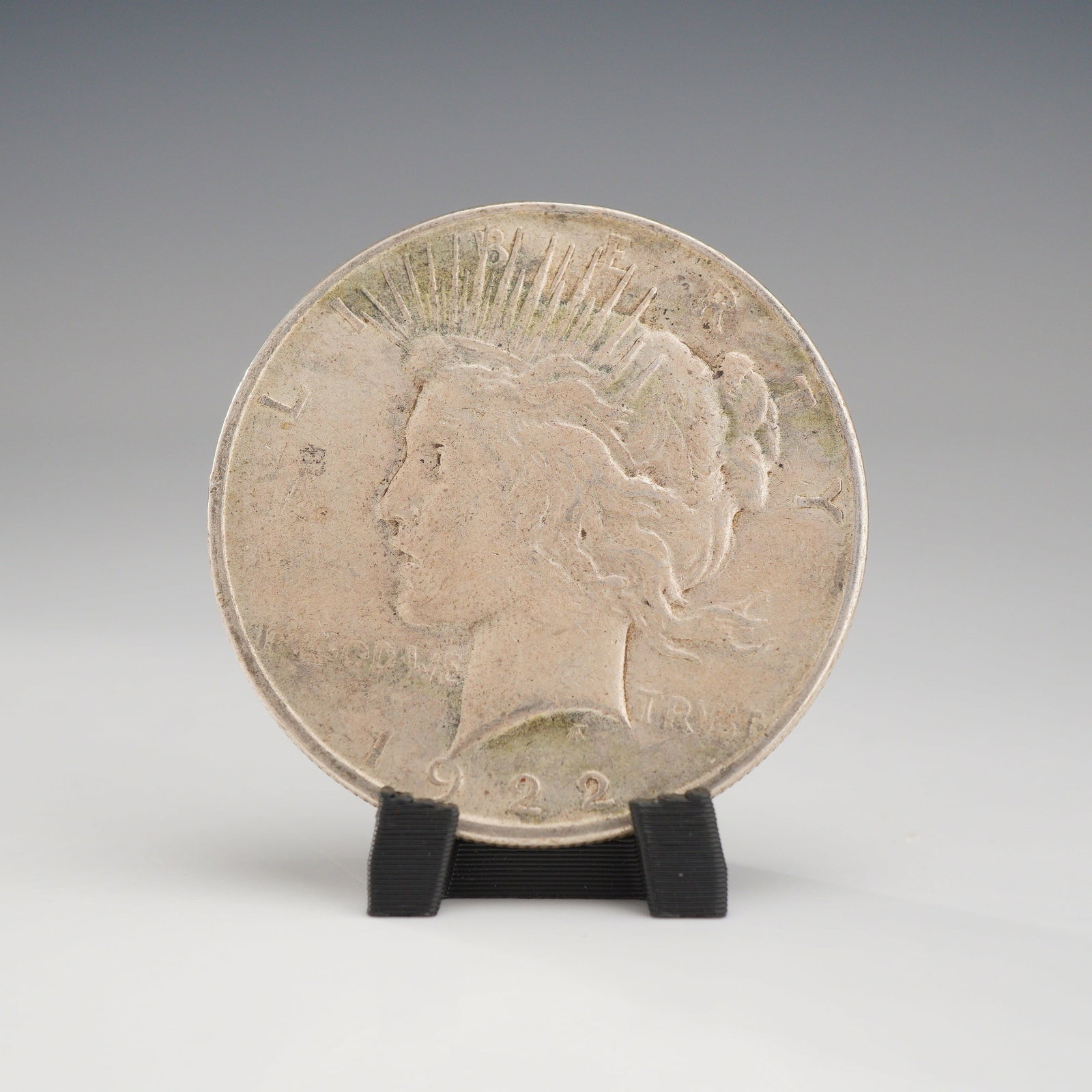 1922 US One Dollar Silver Peace Dollar Coin, Circulated: This 1922 US Peace silver dollar was struck at the Philadelphia mint, indicated by the absence of a mint mark. The coin is composed of 90% silver and 10% copper. The obverse features the Liberty head 