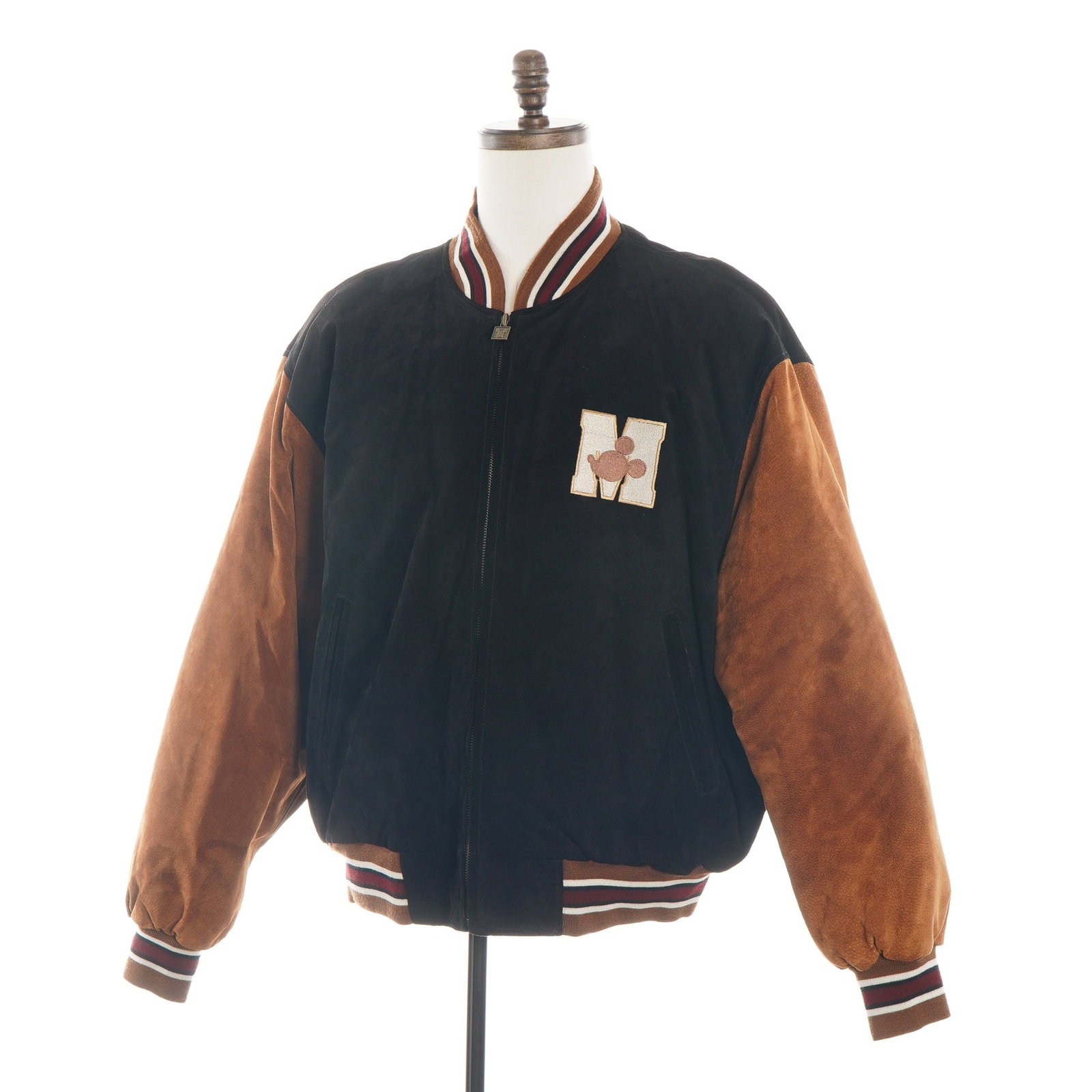 The Disney Store Mickey Mouse Suede Varsity Letterman Jacket Size XL: This vintage varsity-style bomber jacket is a product of The Disney Store, likely dating to the 1990s. The garment features a black suede leather torso with contrasting brown suede raglan sleeves. It 
