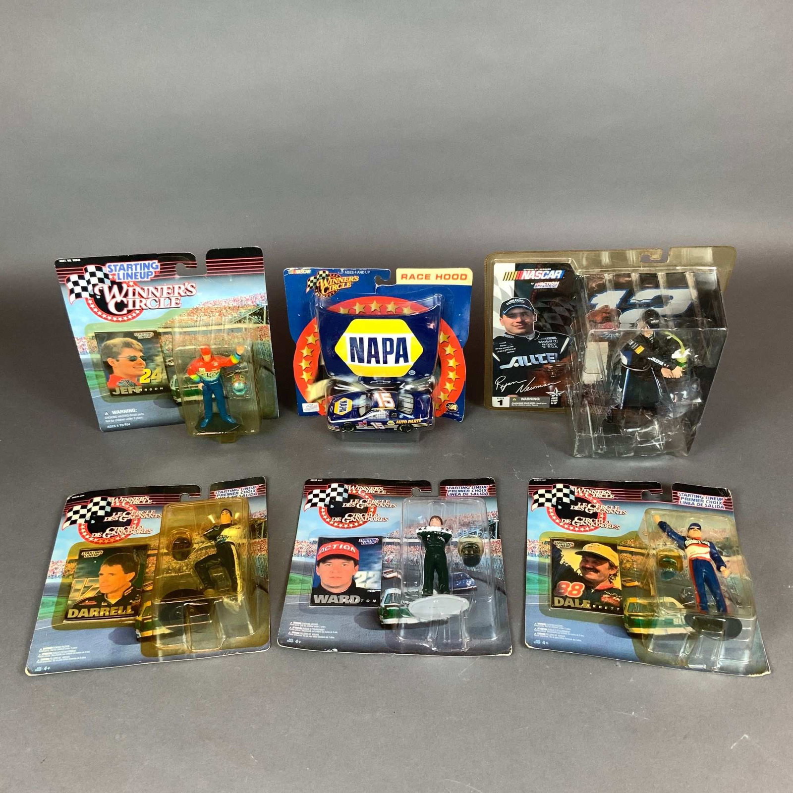 Six Winners Circle and NASCAR Action Figures & Model Cars: A collection of six NASCAR-themed collectibles featuring prominent drivers. The assortment consists of four Kenner Starting Lineup / Winner's Circle figures of Jeff Gordon, Darrell Waltrip, Ward Burto