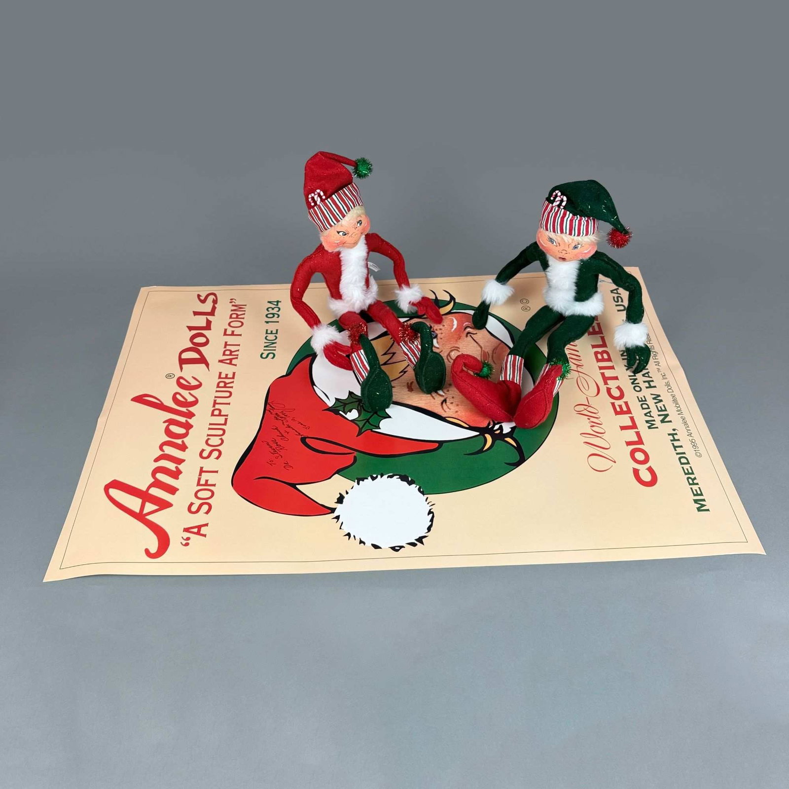 3pc Annalee Dolls Grouping Including Two Large Christmas Dolls and Signed Promotional Poster: This lot features a grouping from Annalee Mobilitee Dolls, Inc. including two large poseable elf dolls and a promotional poster with its original storage tube. The dolls are constructed of felt over a