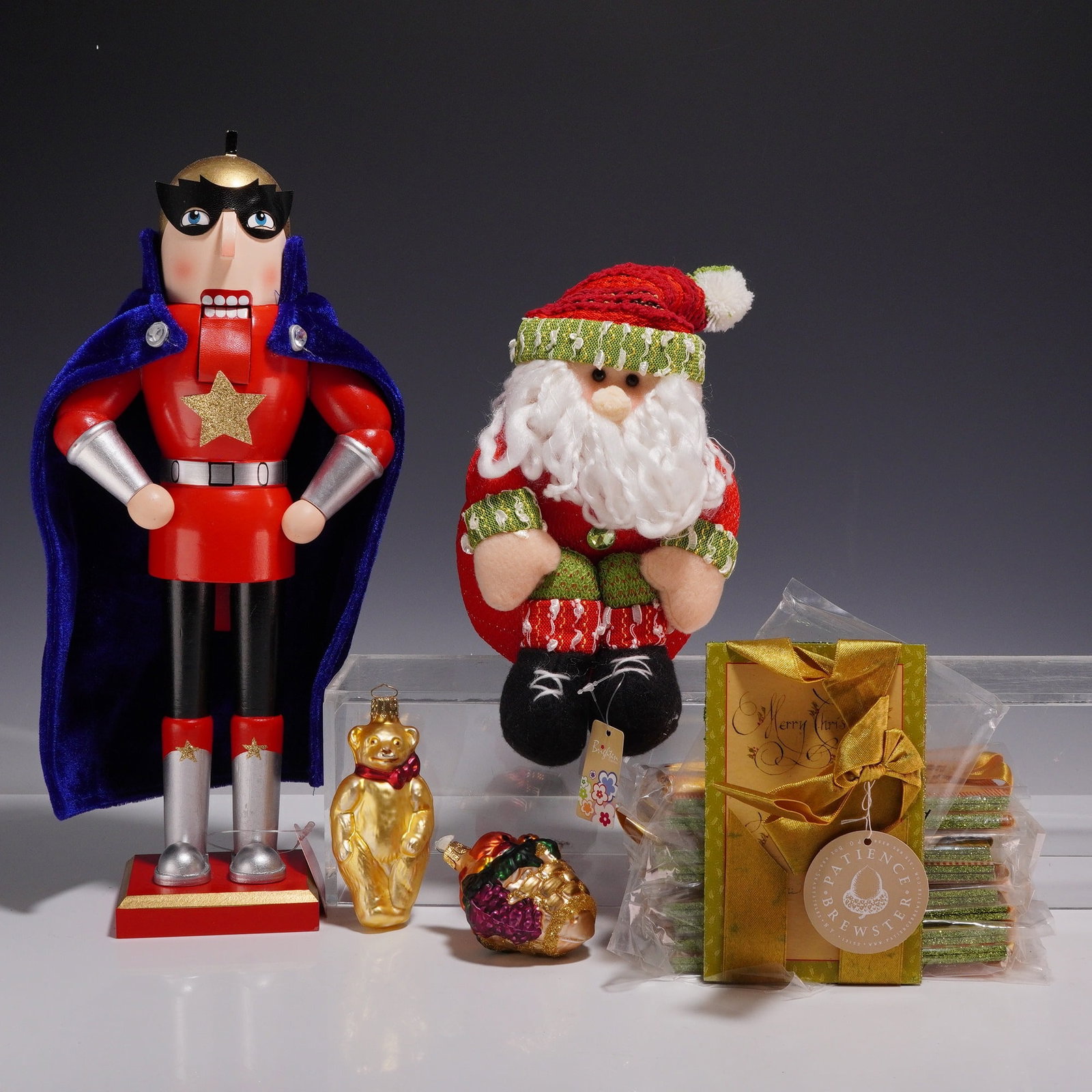 13pc Christmas Grouping Including Macy's Superhero Nutcracker and Sitting Santa Decoration: A thirteen-piece assortment of Christmas-themed decorative items and stationery. This grouping includes a Macy's superhero wooden nutcracker featuring a black mask, red suit with a gold star, and a bl