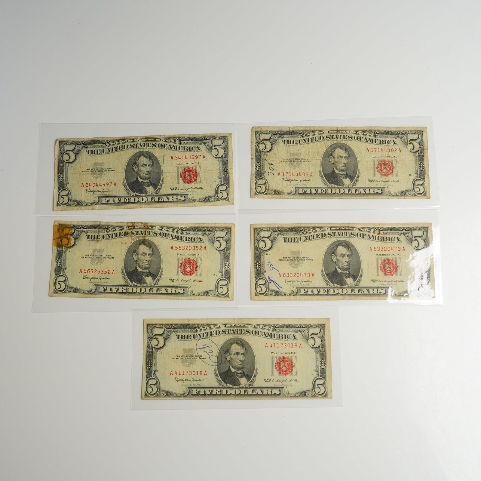 Five 1963 US Five Dollars Red Seal Notes: Each banknote features the portrait of Abraham Lincoln on the obverse and the Lincoln Memorial on the reverse. These notes are distinguished by their red Treasury seals and red serial numbers. Each no