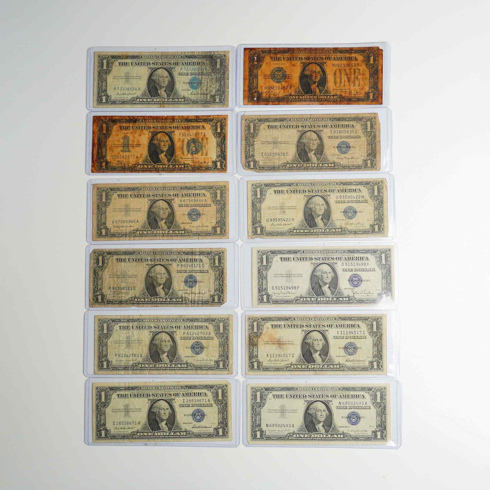 Twelve 1928 - 1957 US One Dollar Silver Certificate Bills: A collection of 12 United States one-dollar silver certificates comprising various series and subseries. The lot includes two Series 1935 A North Africa emergency issue notes, identified by their dist
