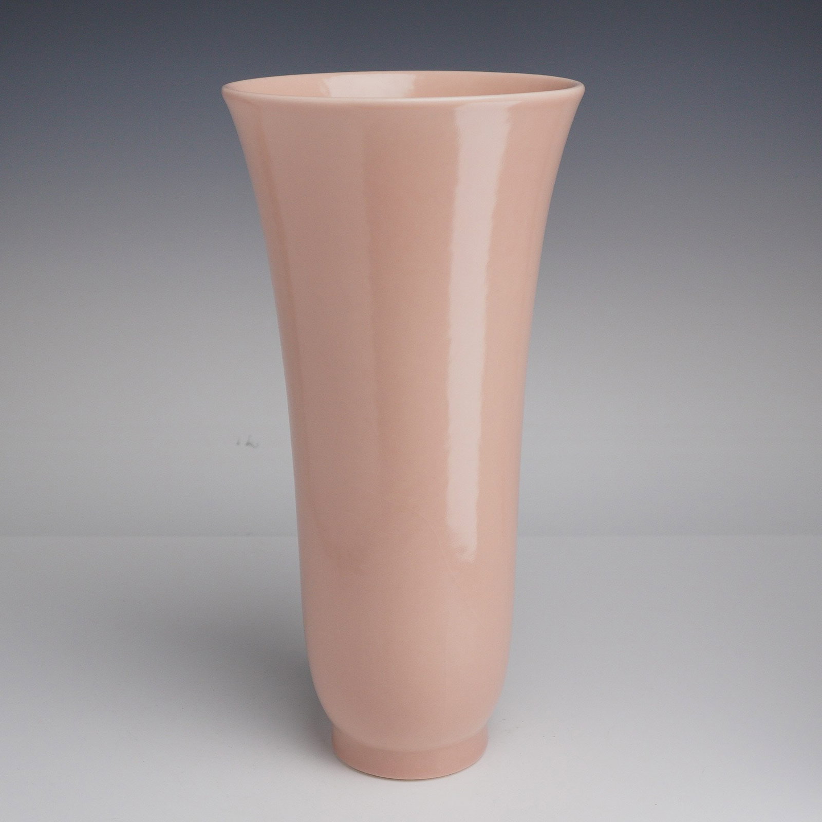 Rookwood Pottery Glazed Vase: This mid-century modern style ceramic vase features a tapered, flared cylindrical form with a subtle footed base. The piece is finished in a uniform, high-gloss pale pink glaze that extends to the int