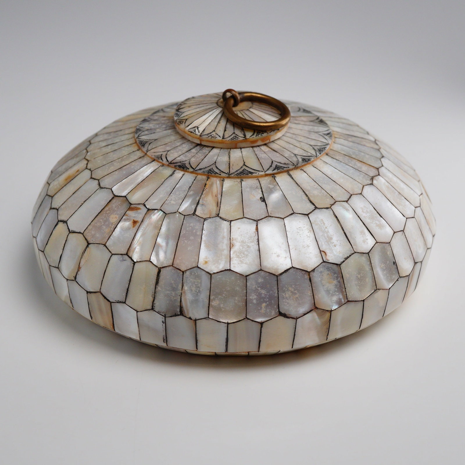 Mother of Pearl Inlay Lidded Box: This low-profile, circular lidded box is constructed of a wood core entirely clad in tessellated mother-of-pearl tiles. The tiles are arranged in radiating concentric patterns across the body and the 
