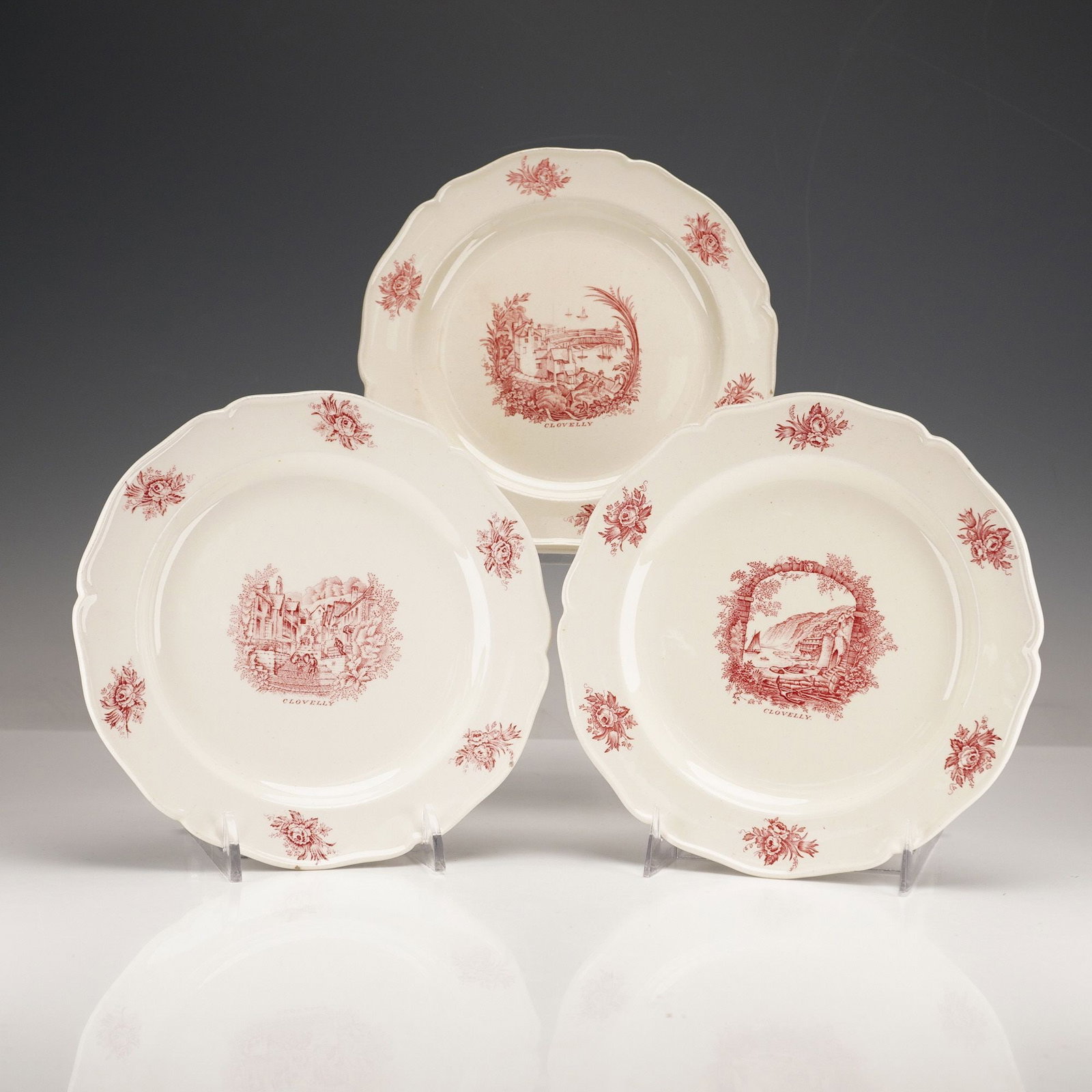 Three Wedgwood 'Clovelly' Plates Designed by Rex Whistler: A set of three Wedgwood 'Clovelly' pattern plates, designed by Rex Whistler. Each ceramic plate features a scalloped rim and is decorated with red transferware on an off-white ground. The border displ