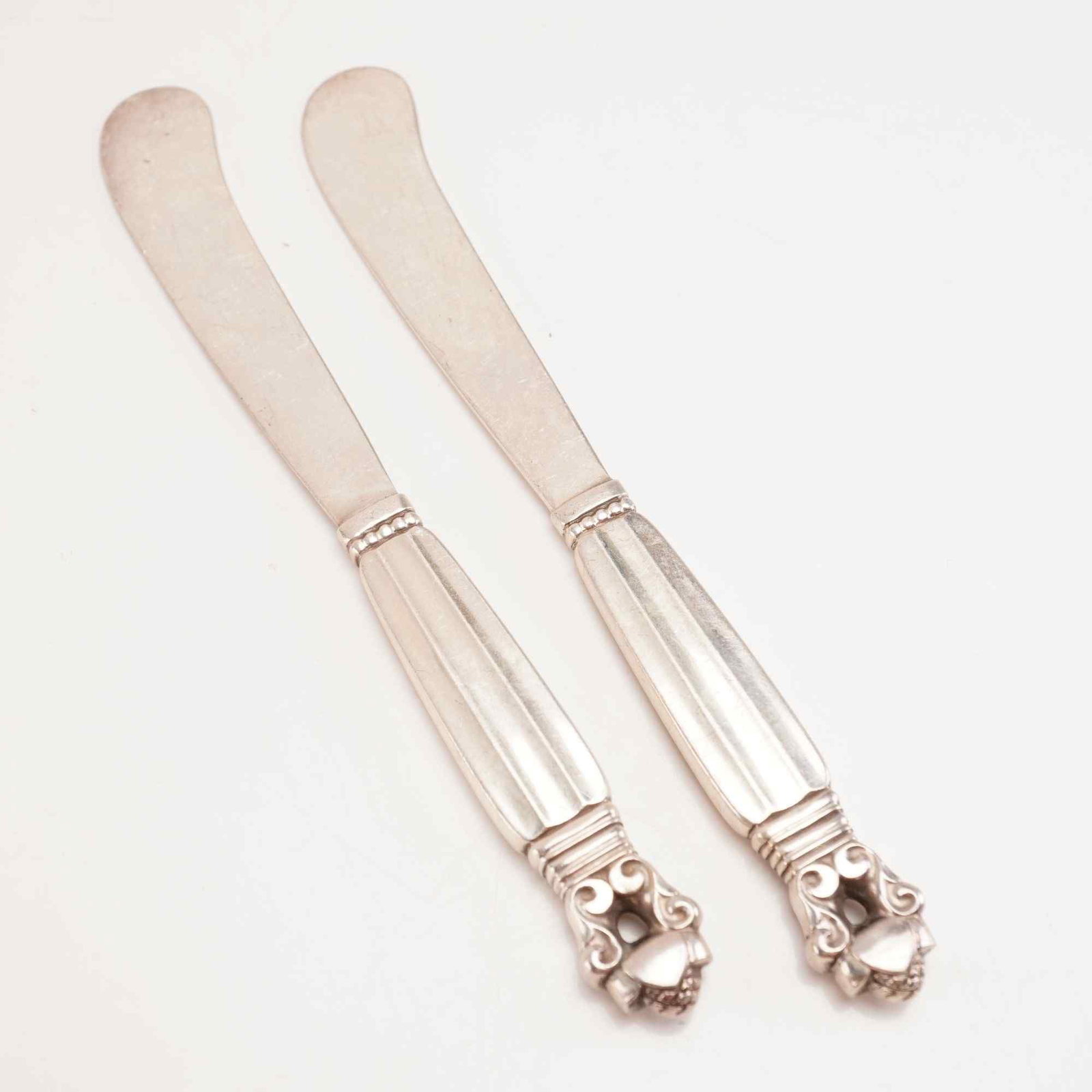 2pc George Jensen Sterling Silver Butter Spreaders, Acorn: Two-piece set of Georg Jensen sterling silver butter spreaders in the Acorn pattern. Designed in 1915 by Johan Rohde in collaboration with Georg Jensen, the Acorn pattern combines Art Nouveau and Art 