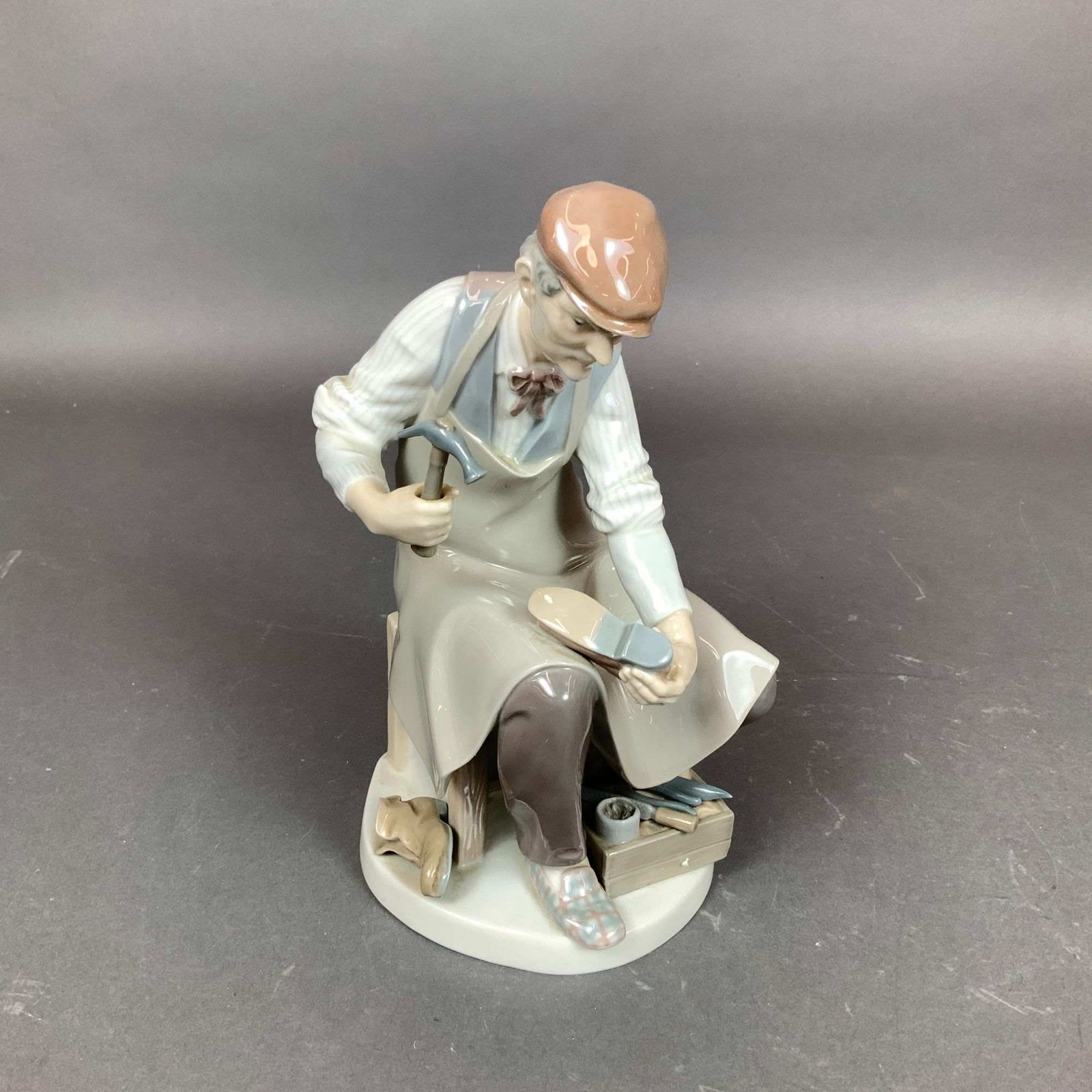 Lladro Porcelain Figurine, The Cobbler 01004853: This Lladro porcelain figurine, titled The Cobbler (Spanish title: El Zapatero) and identified by item number 01004853, was designed by sculptor Salvador Furio and produced between 1974 and 1994. The 