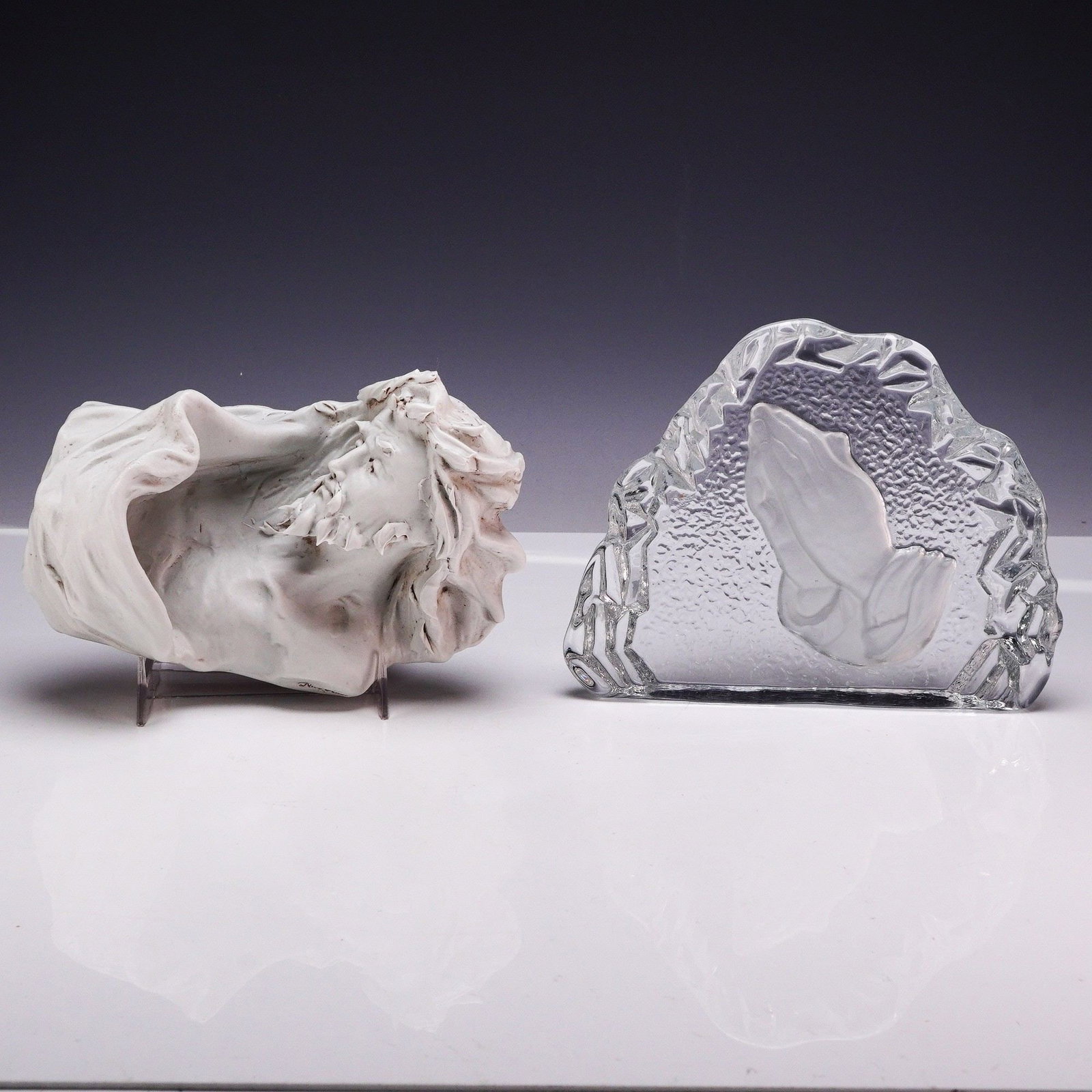2pc Religious Figures, Nico Venzo Ceramic Figurine and Prayer Hands Glass Plaque: This lot features two religious-themed decorative pieces consisting of a signed ceramic bust and a molded glass relief plaque. The first is a matte white bisque porcelain bust depicting Jesus Christ w