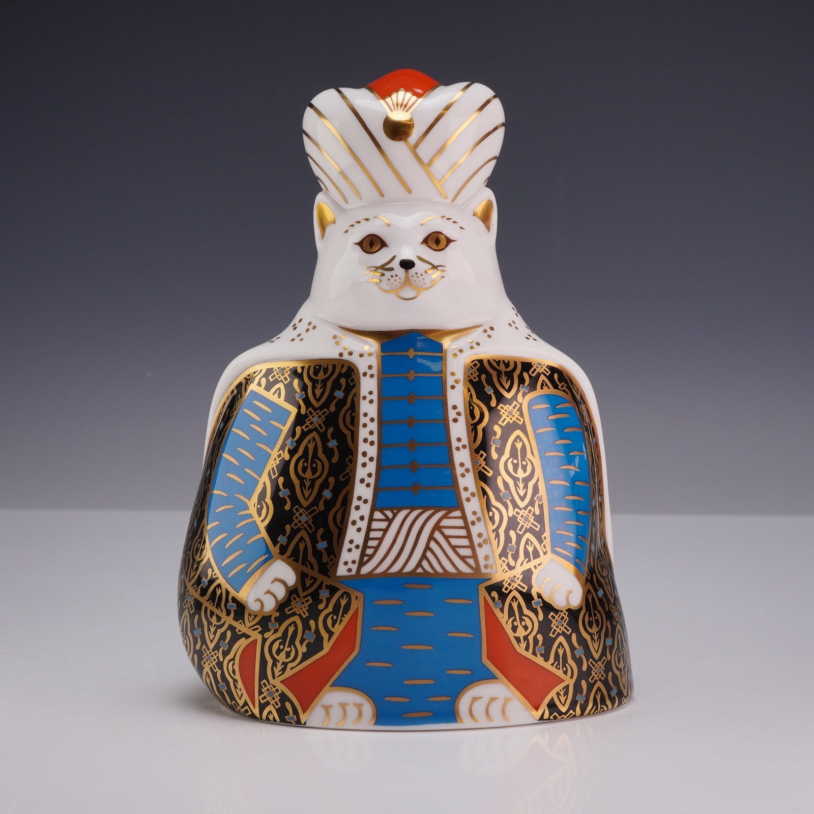 Royal Crown Derby Bone China Paperweight Figurine, Royal Cats Persian: A Royal Crown Derby fine bone china figurine from the Royal Cats collection titled Persian. The stylized white cat is depicted in a seated pose wearing elaborate Persian-style courtly attire. The cost