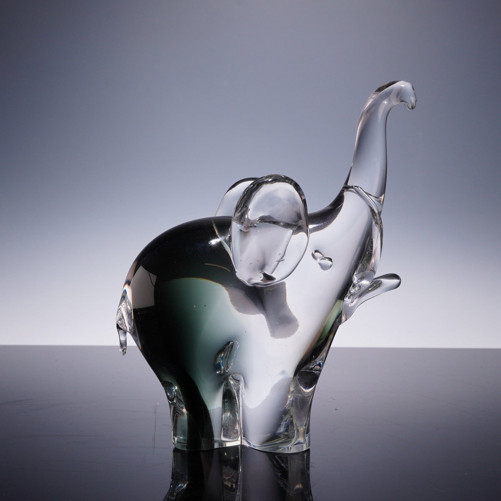 Murano Style Hand Blown Art Glass Elephant Figurine: This is a Murano-style hand blown art glass elephant figurine, characterized by a mid-century modern aesthetic. The piece depicts an elephant in a trumpeting pose with its trunk raised and one front