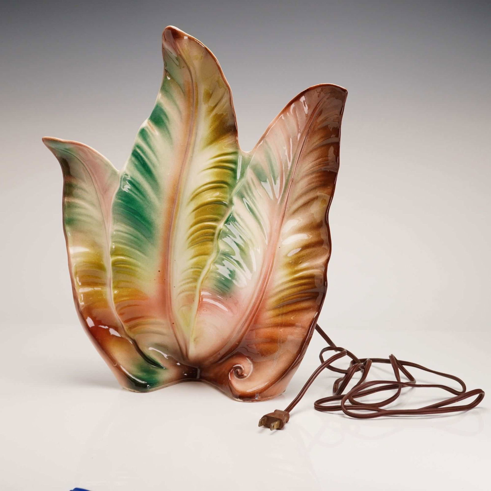 Lane & Co. Tropical Leaf Ceramic TV Lamp: A mid-century modern ceramic lamp produced in Van Nuys, California, in 1958. It features a palm leaf shape with a cream-colored body and accents in shades of green, pink, and brown. It is marked on