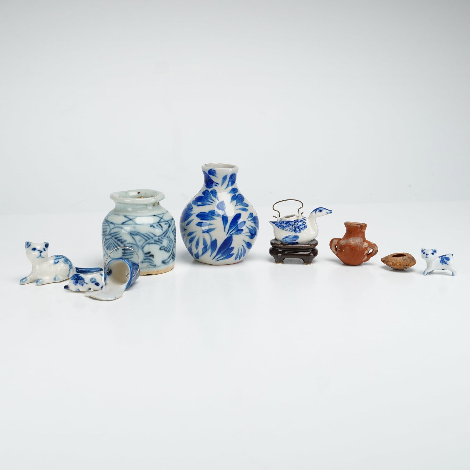 Lot of 10 Porcelain and Pottery Miniatures Including Animal Figures and Vases: A collection of ten miniature objects crafted from porcelain and pottery. The lot includes five blue and white porcelain animal figures and vessels: a reclining cat, two standing kittens, and a
