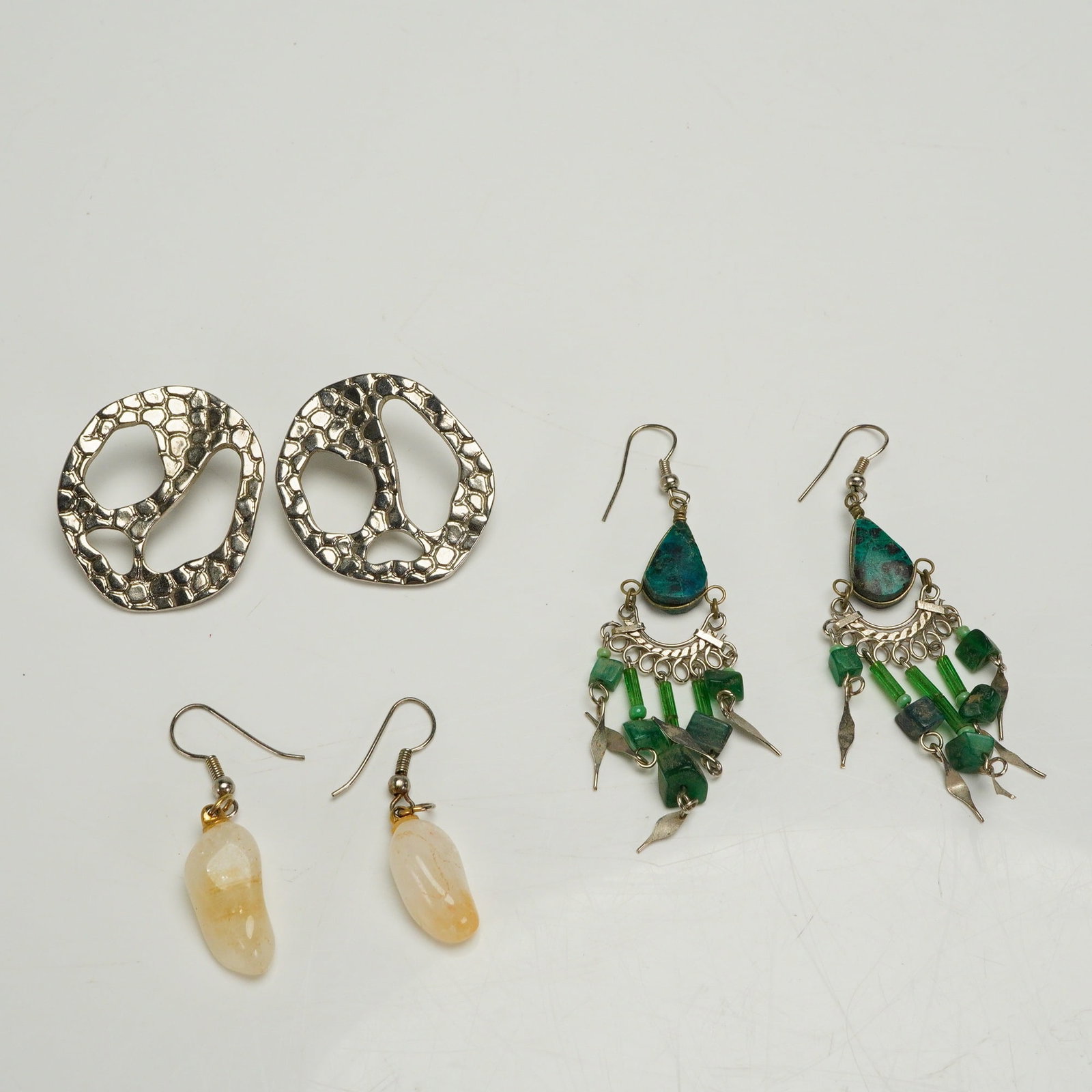 A Collection of Three Pairs of Assorted Costume Earrings: A collection of six individual earrings, forming three distinct pairs of costume jewelry. The first pair consists of large, abstract, openwork stud or clip-on earrings crafted from silver-tone metal, 
