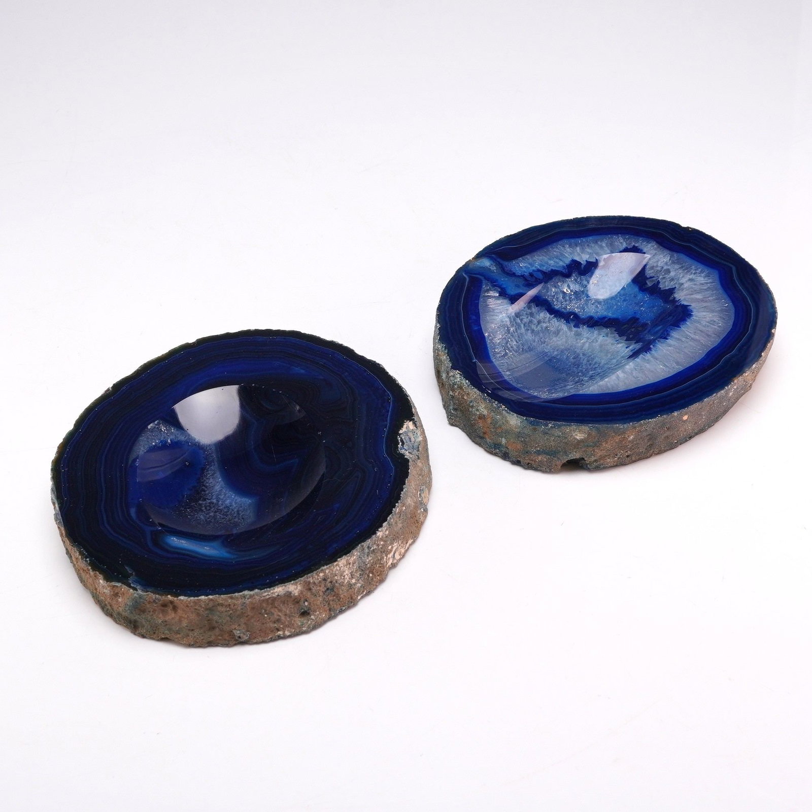 2pc Blue Agate Geode Mini Bowls: A pair of decorative mini bowls crafted from blue agate geode slices. Each piece features a shallow, ground-out central depression designed for use as a decorative bowl or catchall. The stone