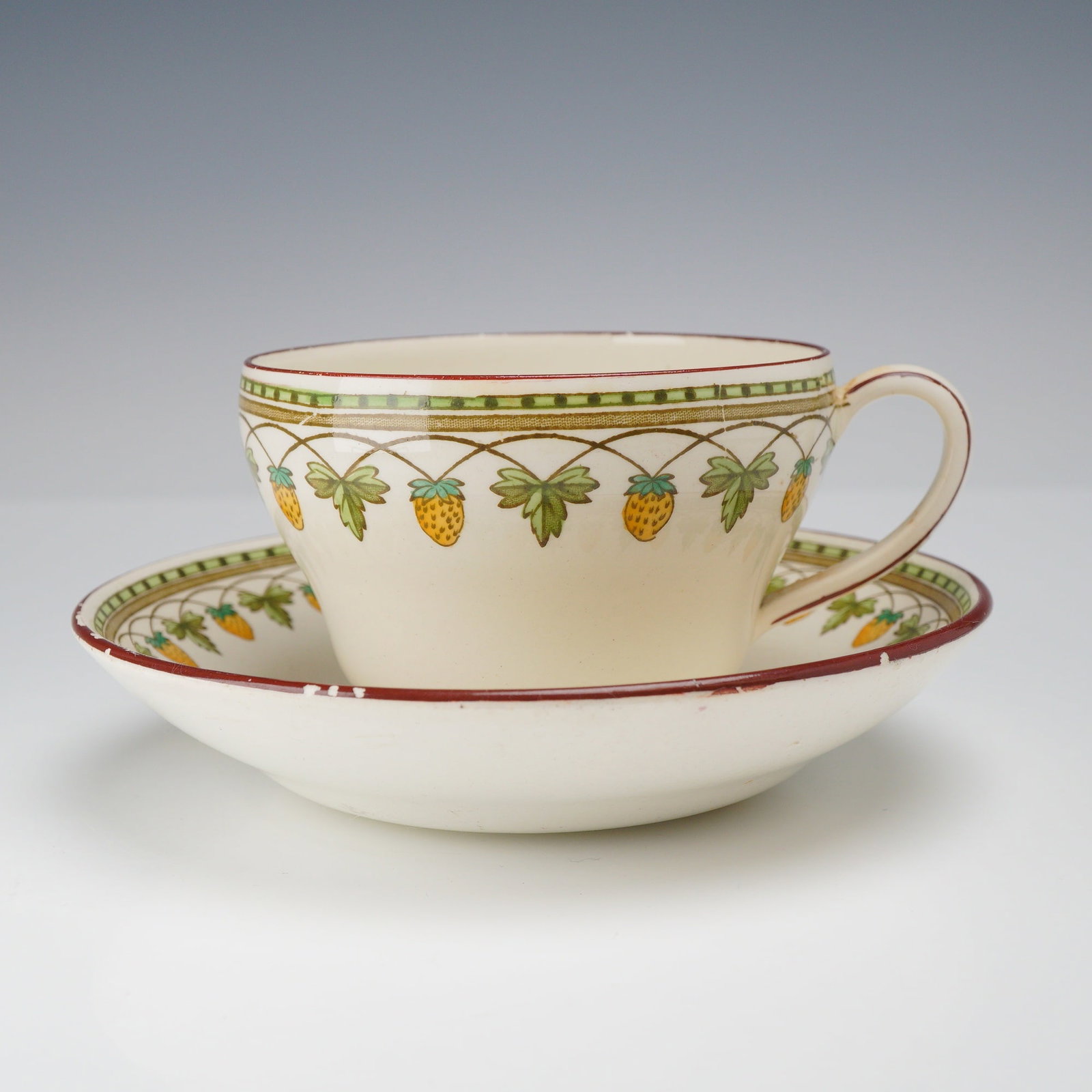 Wedgwood Creamware Teacup and Saucer for W.H. Plummer and Co., Strawberry Fruit Pattern: This teacup and saucer set is crafted from creamware, a type of refined earthenware produced by Wedgwood at the Etruria factory in England. The set features the Strawberry Fruit pattern, consisting of