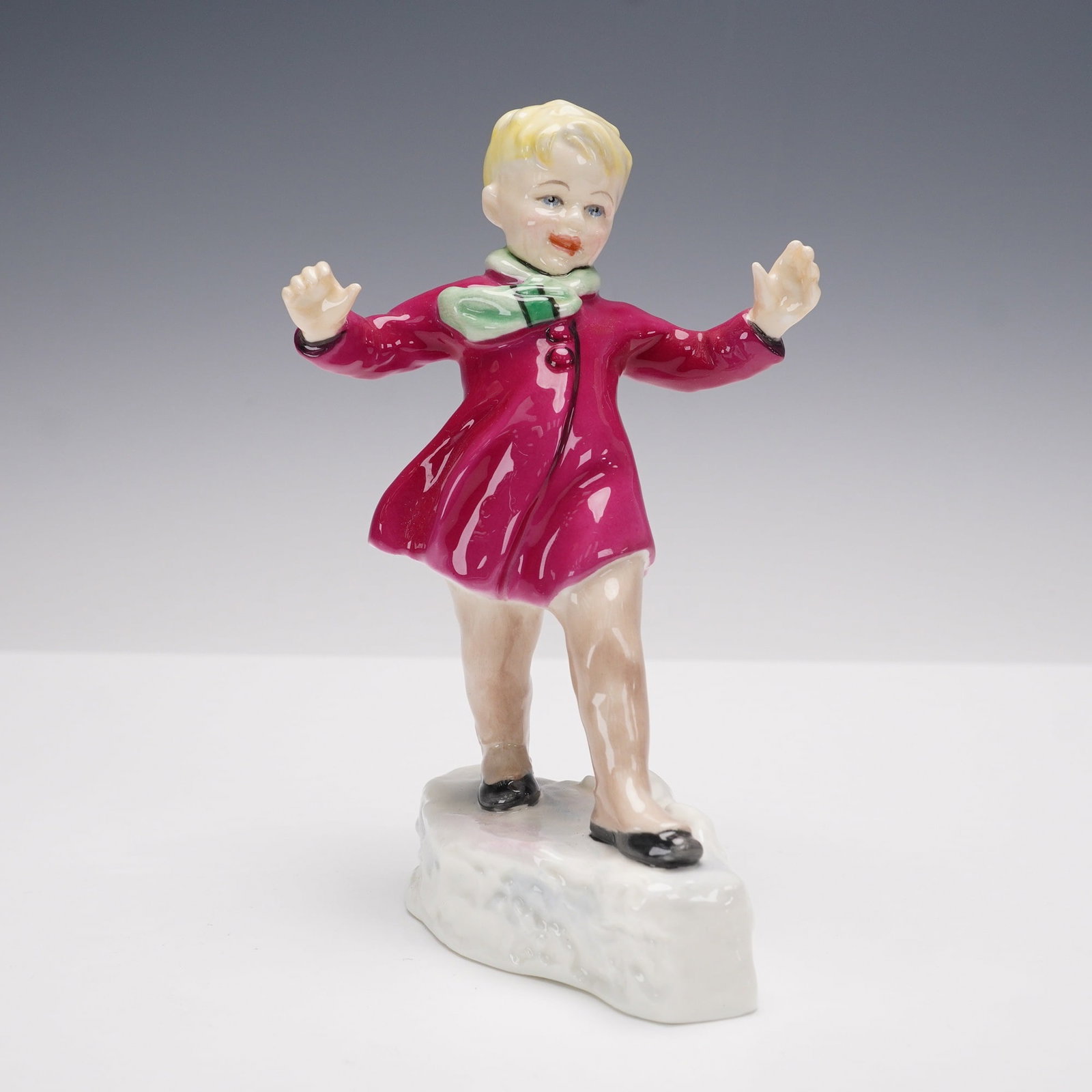 Royal Worcester Figurine, January 3452: Royal Worcester bone china figurine titled January, model 3452, modeled by F. G. Doughty. The piece depicts a young child in a bright red coat with green scarf, balancing playfully on a snowy base. Fi