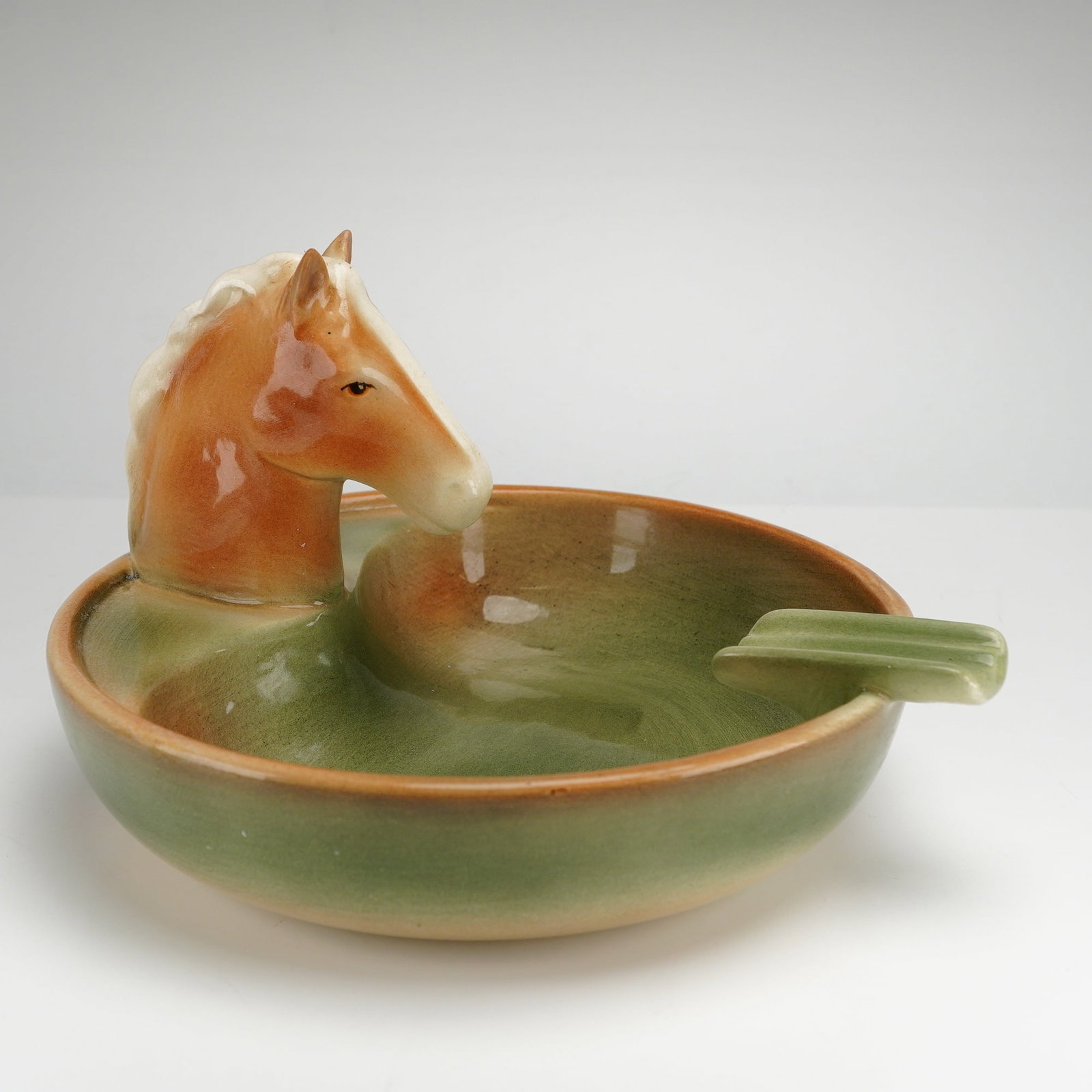Goldscheider Porcelain Horsehead Ashtray: A mid-century modern Goldscheider porcelain horsehead ashtray produced by Goldscheider-Everlast Corp. The circular dish features a sculptural horse head protruding from the interior wall, rendered in