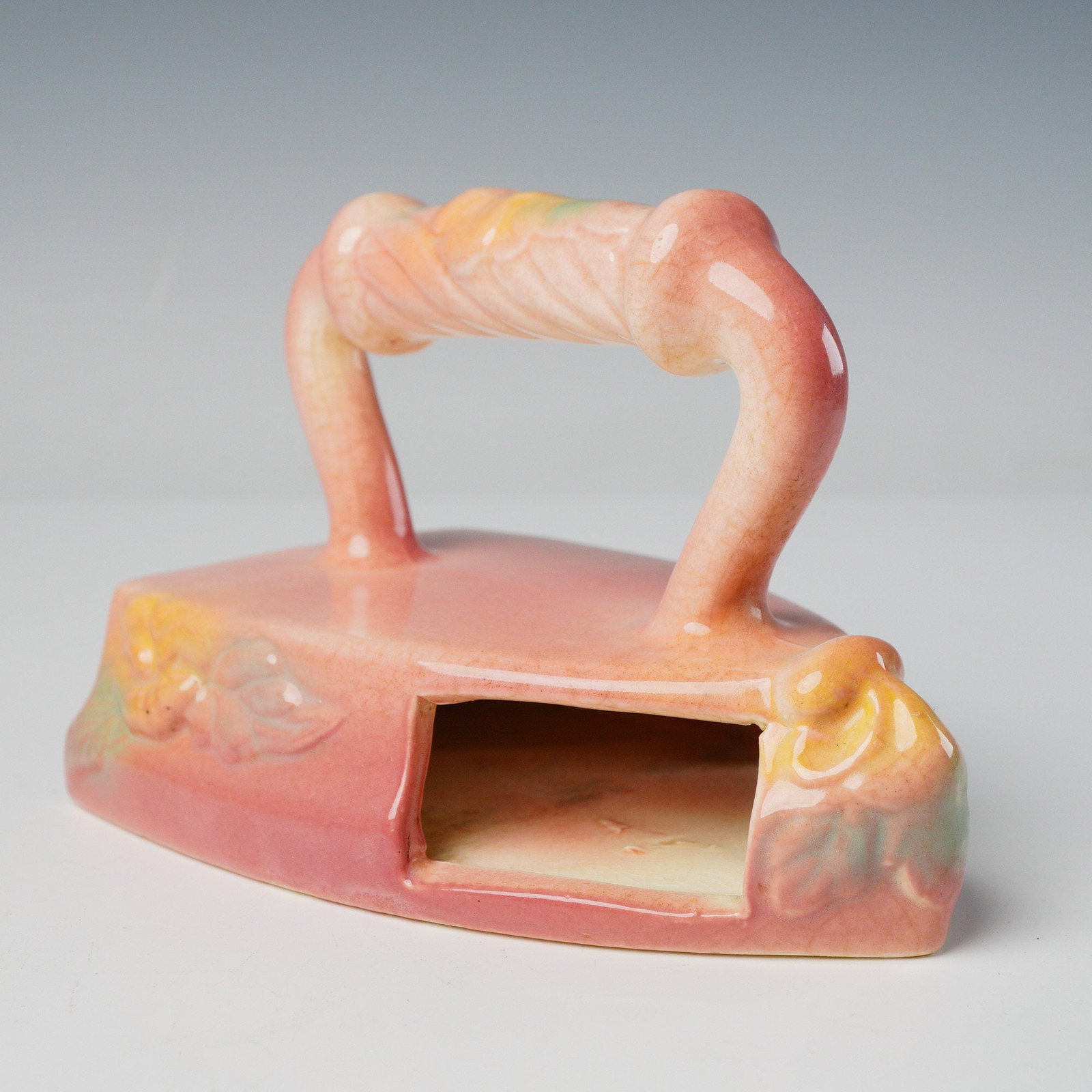 Hull Pottery Flat Iron Wall Pocket: Crafted from glazed earthenware, features a primary finish in salmon pink or coral, accented with swirls of yellow, cream, and pale mint green on the highly stylized handle and the relief-molded