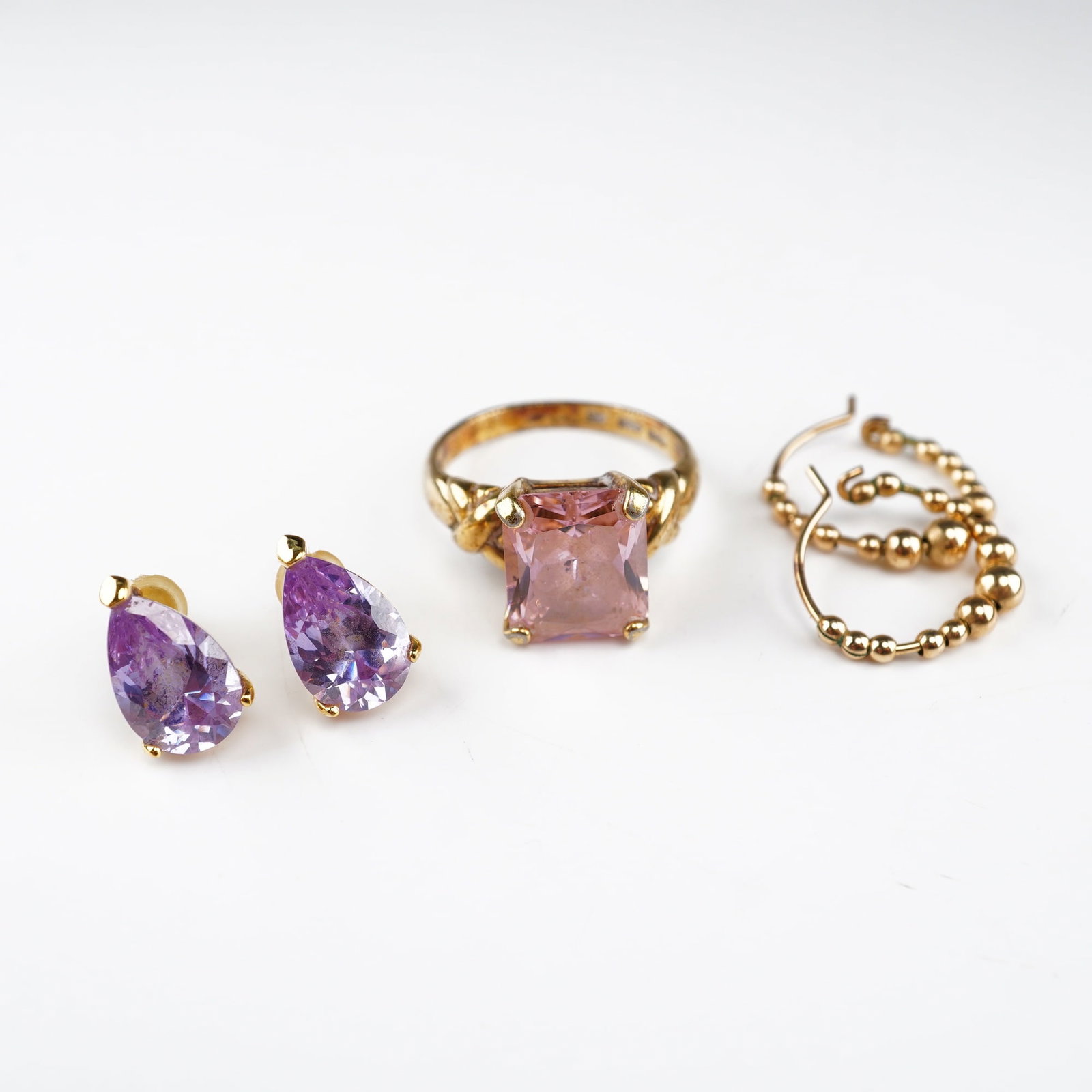 A Collection of Five Pieces of Gold Plated Jewelry Including a Pink Gemstone Ring and Earrings: This assortment of five pieces of gold-plated jewelry features faceted gemstones and classic designs. The collection includes one gold-tone ring with a large emerald-cut pink gemstone held in a four-p