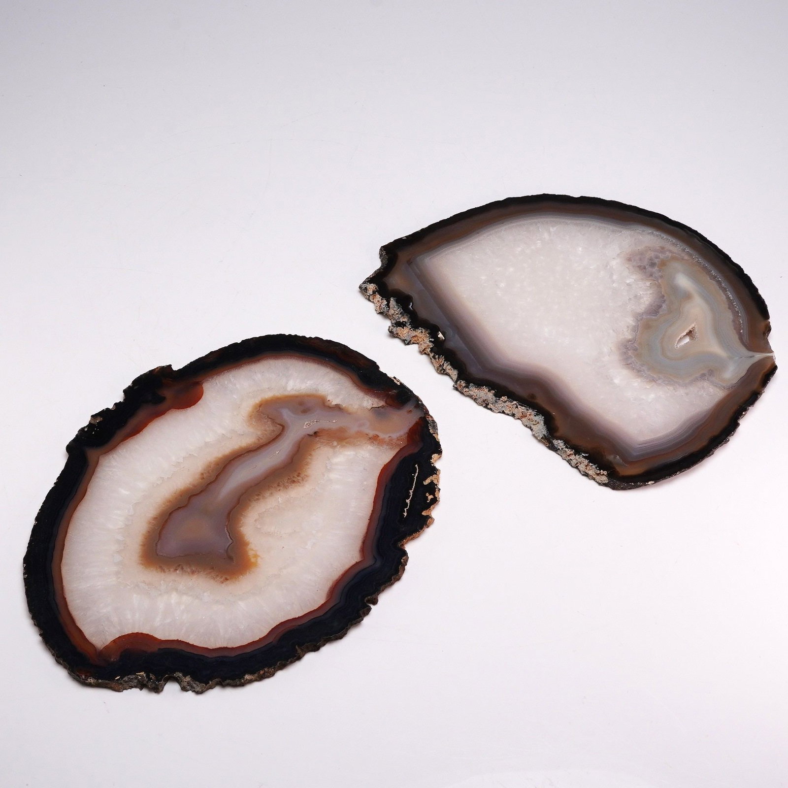 2pc Brazilian Banded Agate Slices: This lot consists of two polished Brazilian agate slices featuring distinct concentric banding and natural geode formations. The specimens exhibit a color palette ranging from deep charcoal and black 