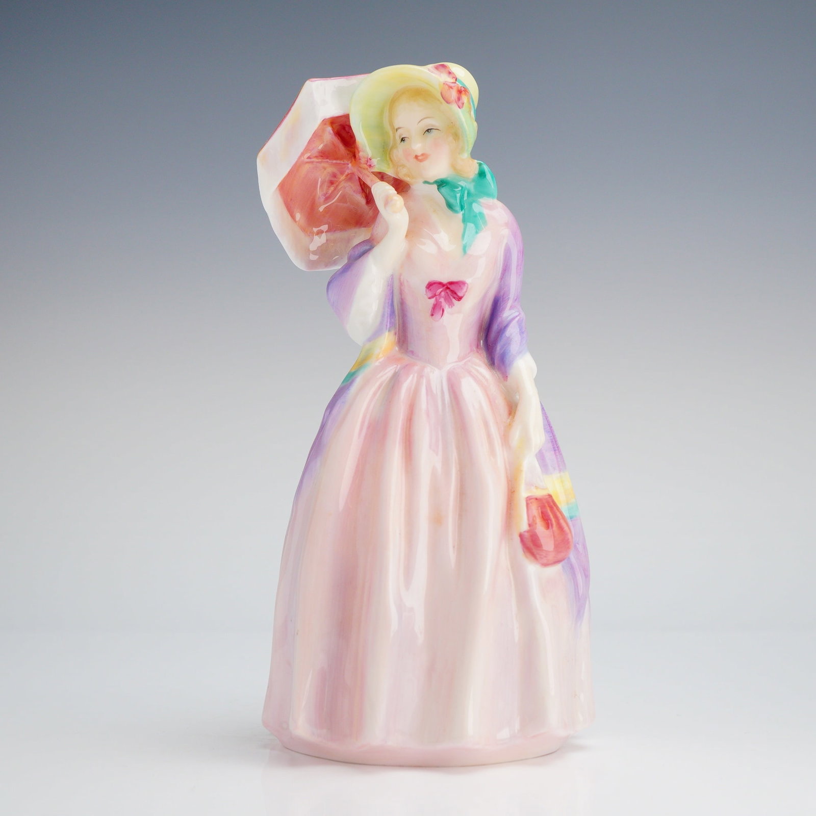 Royal Doulton Figurine, Miss Demure HN1402: The piece depicts a lady in early 20th-century style, characterized by a broad-brimmed hat, a flowing pink dress, and a colorful shawl. She is shown holding a coral-colored parasol and a matching hand