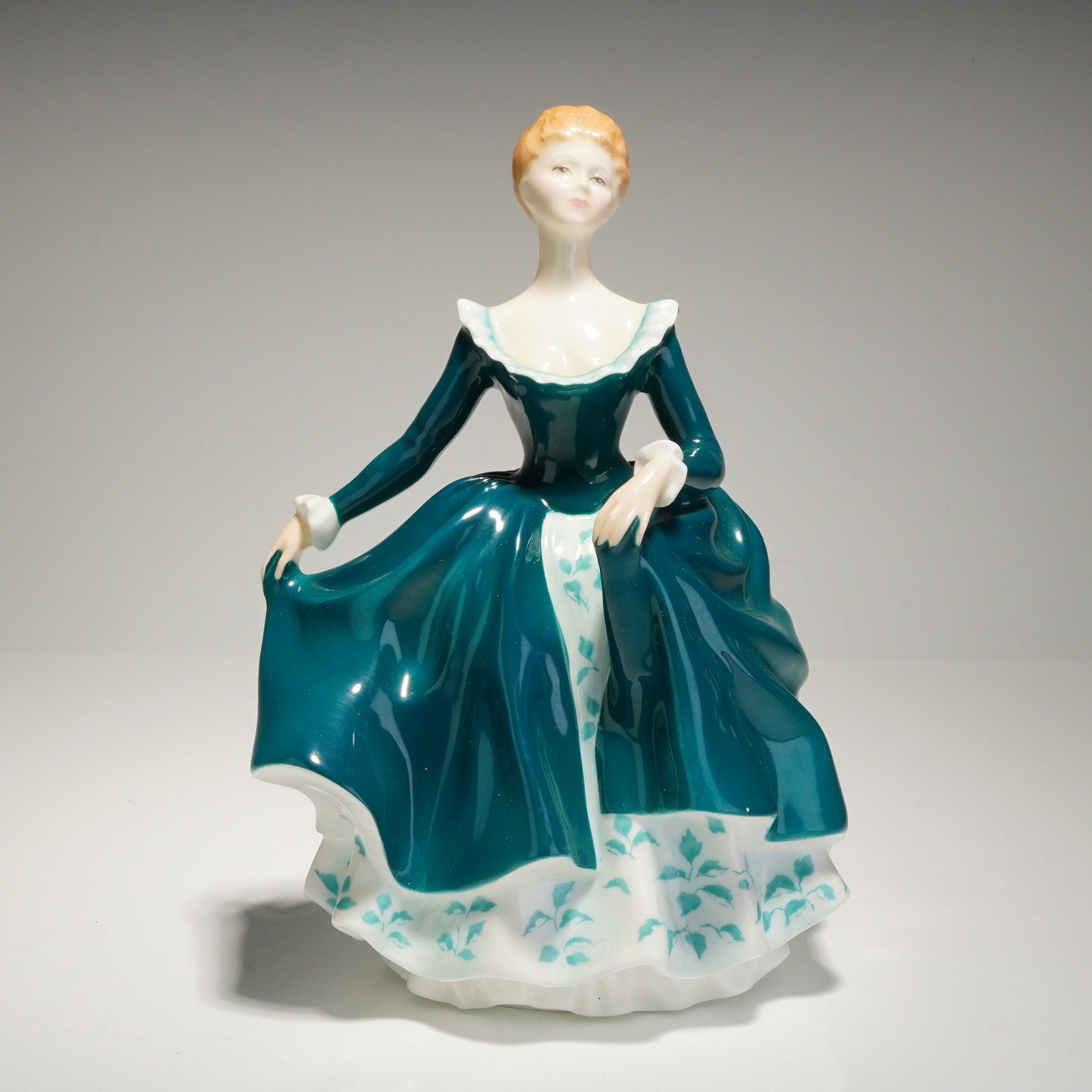 Royal Doulton Porcelain Figurine Janine HN2461: A single Royal Doulton porcelain figurine titled 'Janine,' model number HN 2461. The figure depicts a standing woman with auburn hair, dressed in a voluminous, highly glossy gown of deep teal. The dre