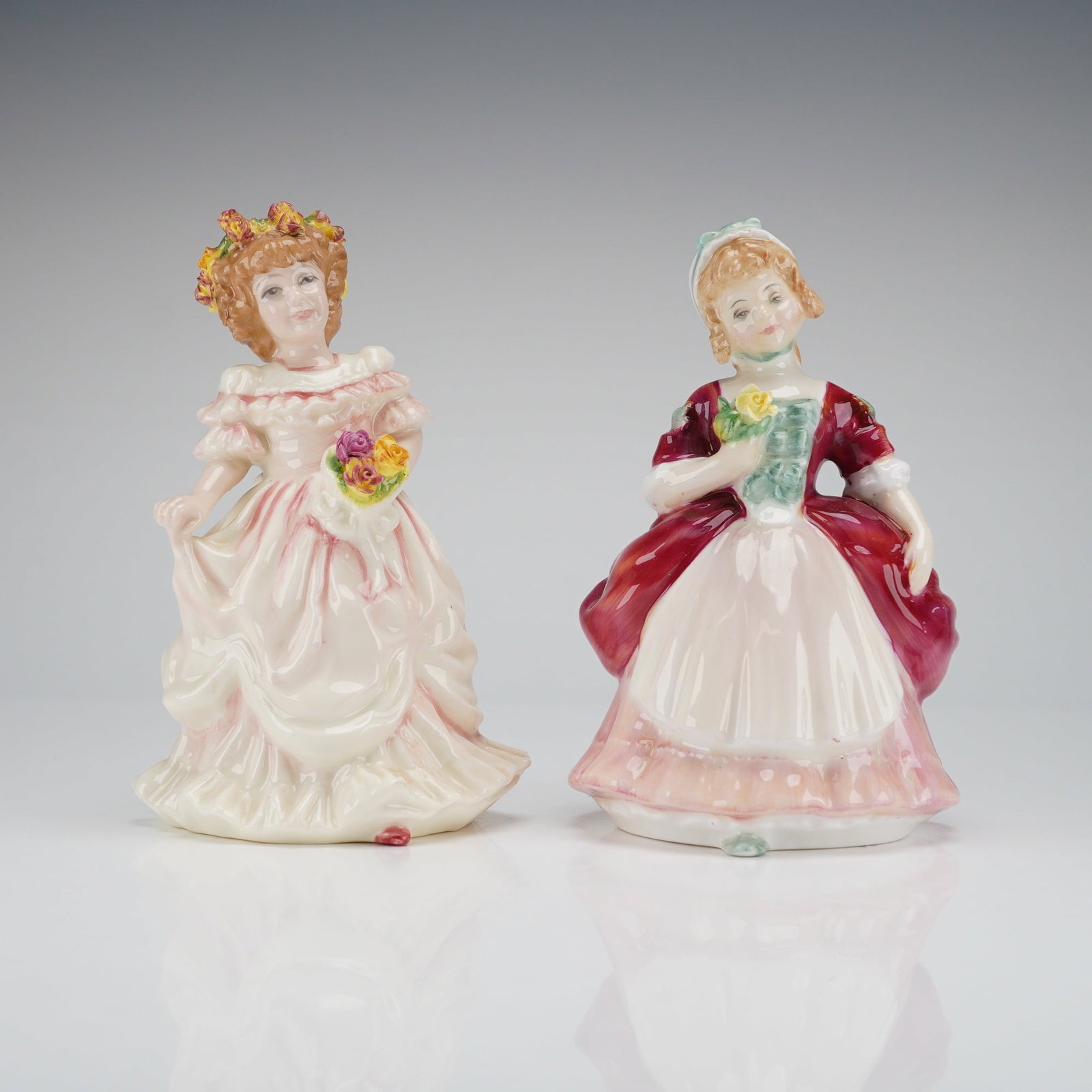 2pc Royal Doulton Porcelain Figurines Bridesmaid and Valerie: The first figurine is identified by the base stamp as Bridesmaid Flower Girl HN 3476, copyrighted 1993. This figure is depicted in a pale pink and white period costume and wears a wreath of yellow and