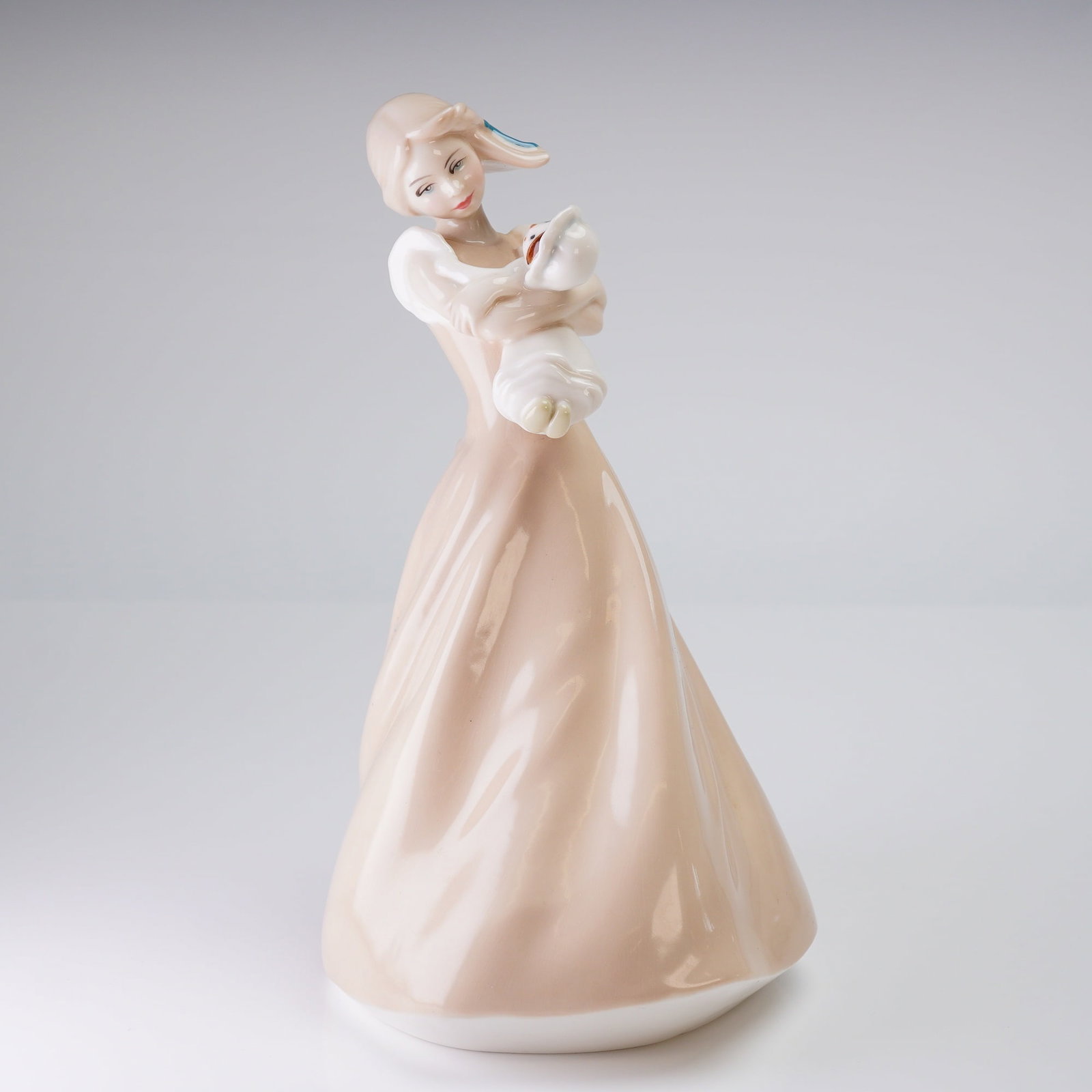 Royal Doulton Figurine, Reflections Dreaming HN3133: The piece depicts a standing woman dressed in a flowing, blush-pink gown holding a swaddled infant. The figurine features a modern, elegantly stylized aesthetic with pastel coloration and a glossy fin