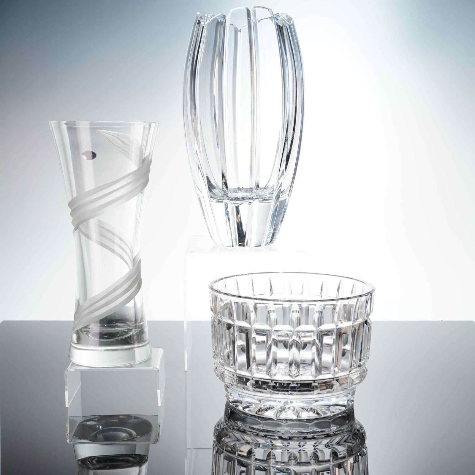 3pc Crystal Vases and Bowl: This collection features three pieces of clear lead crystal tableware. The first item is a contemporary-style vase with three frosted ribbon-like bands spiraling diagonally around the body, finished