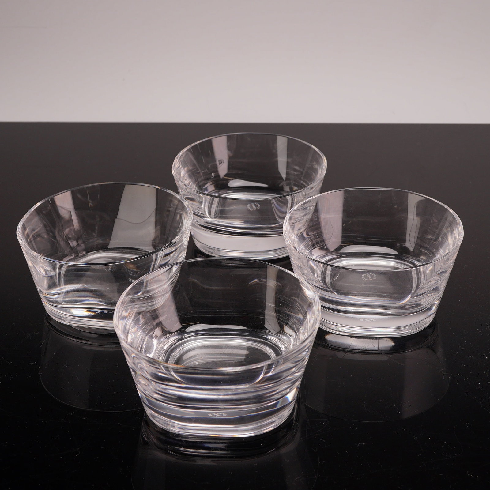 Set of Four Sevres Cristal Bowls: Each vessel features a square-to-round architectural form with flaring sides. The lower portion of each bowl is decorated with multiple deep, horizontal wheel-cut bands, while the upper section is